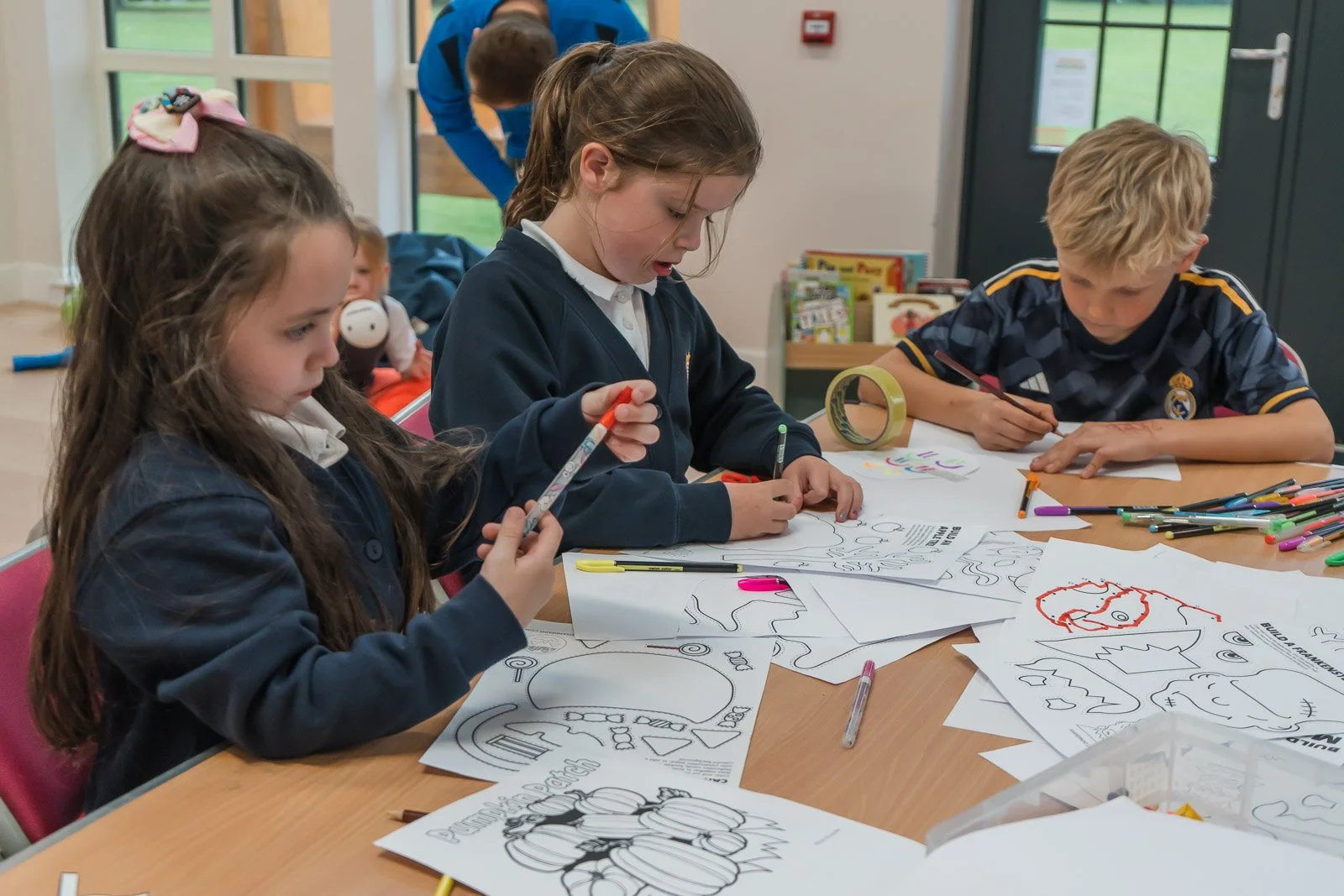 Three children are colouring Halloween-themed worksheets at DDYP in Doune.
