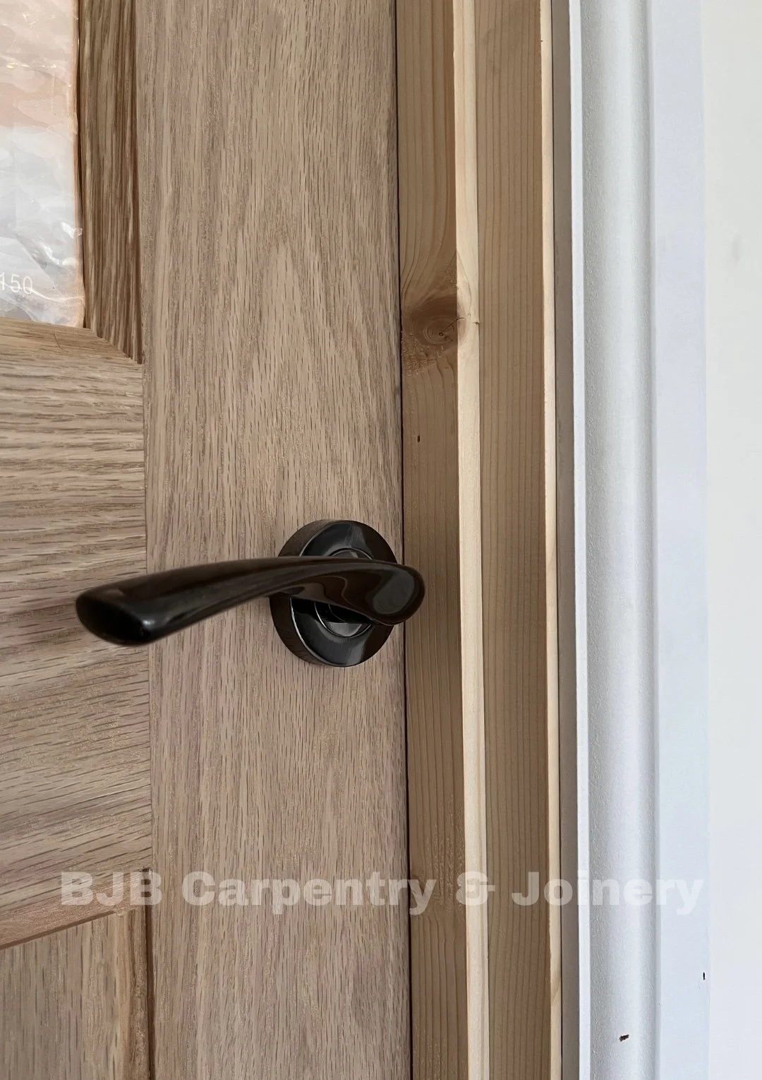 A black door handle on a wooden door with light wood panels and a white wall in the background.