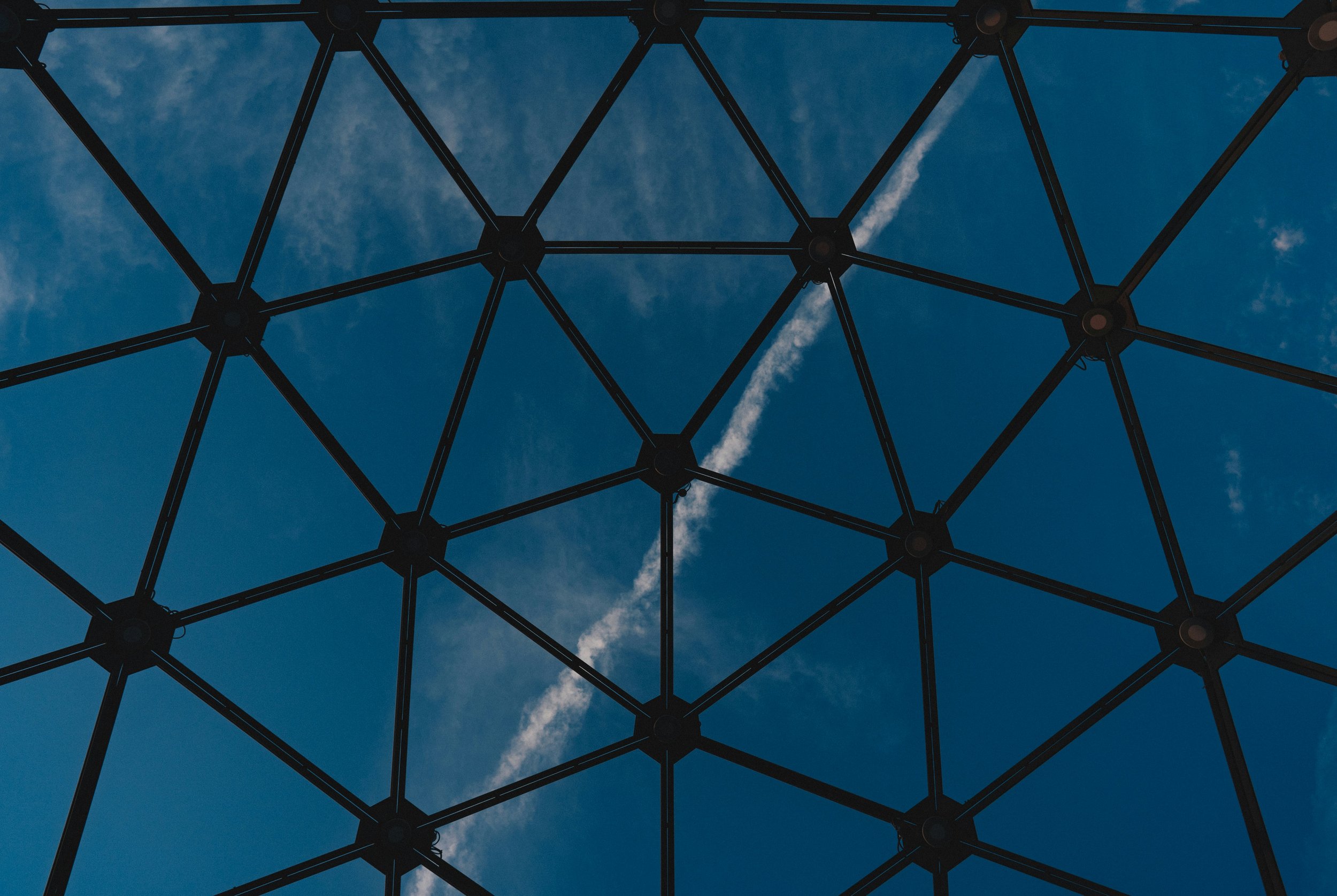 Close-up view of a geometric metal lattice structure against a blue sky with wispy clouds.