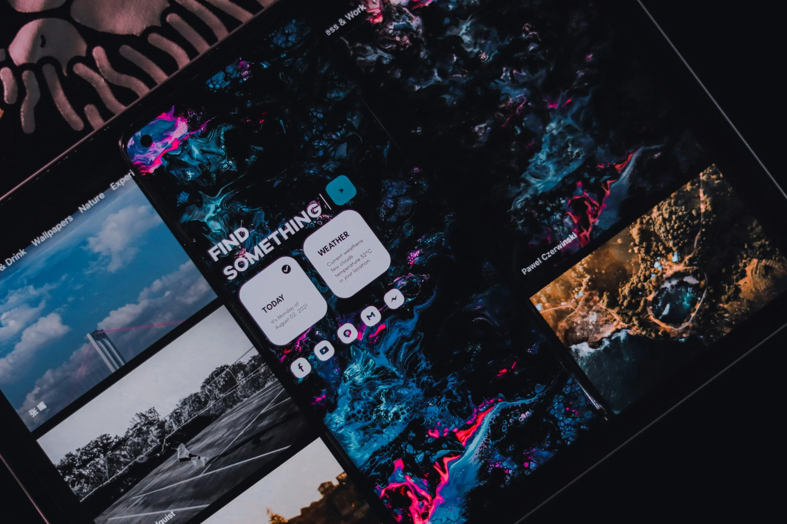 Multiple smartphone screens displaying colorful abstract wallpapers and weather information, arranged on a dark surface with a zebra-patterned cloth nearby.