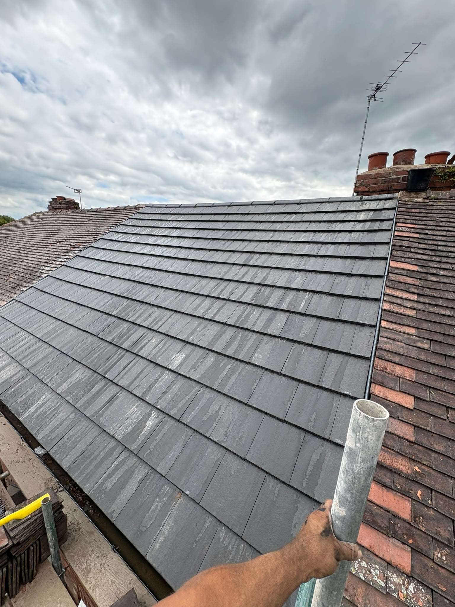 Roof with new slate tiles being installed, hand holding a pipe, overcast sky