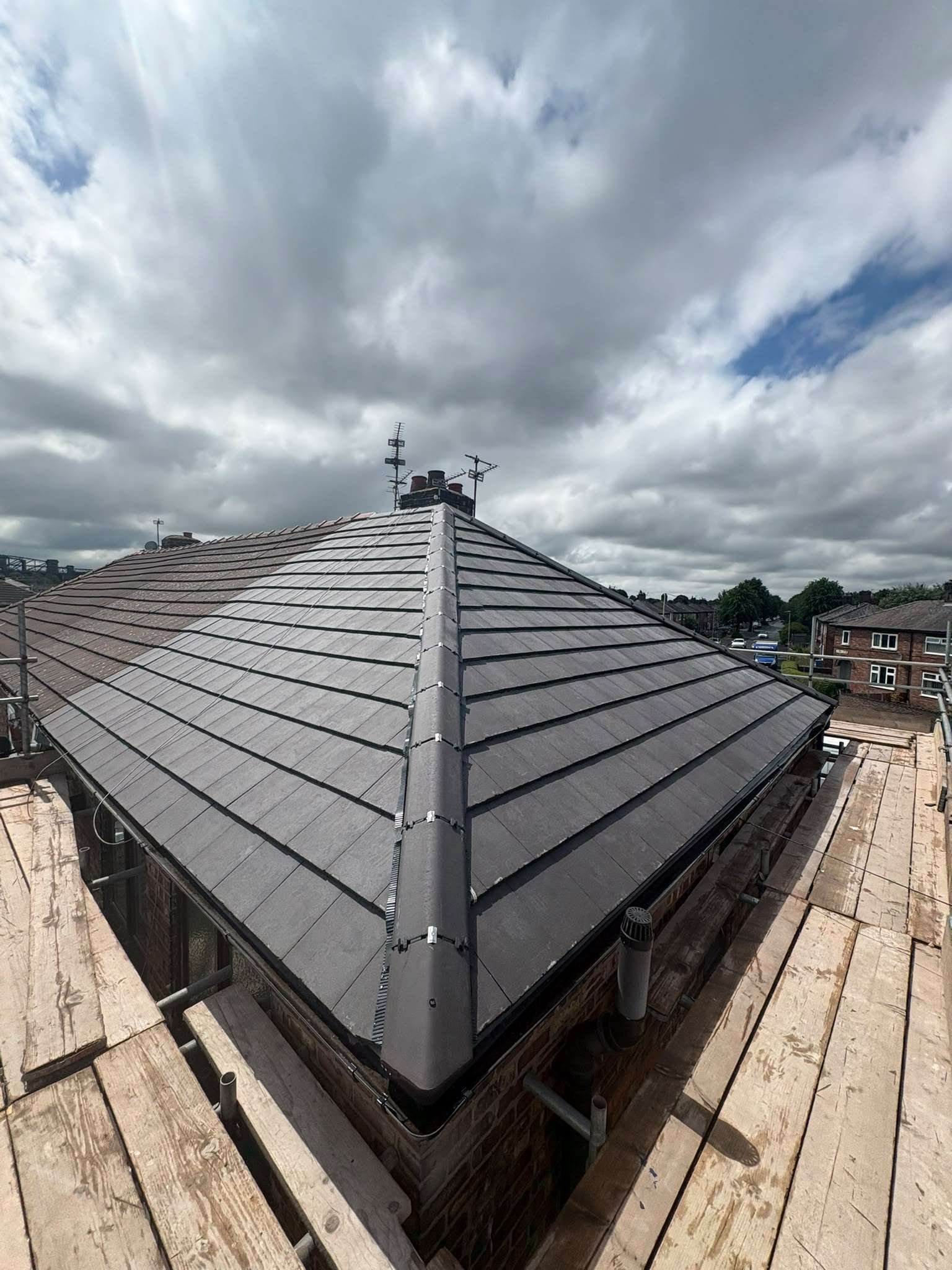 View of a residential rooftop with a metal roof, antennas, and ventilation pipes, under a cloudy sky during daytime.