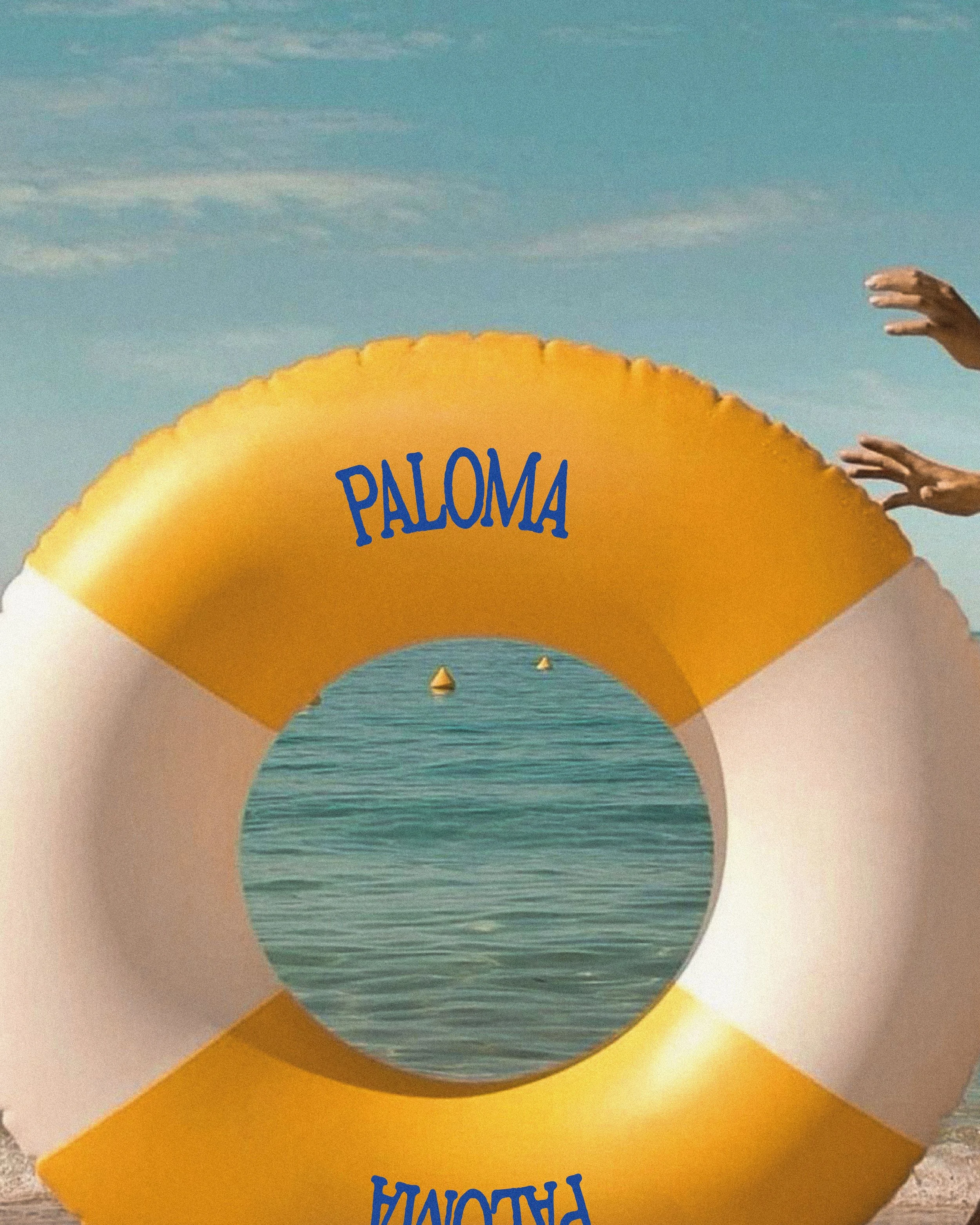 Un ballon jaune avec le nom 'Paloma' écrit dessus, placé devant un fond d'eau et de ciel avec des nuages, et des mains qui touche le ballon.