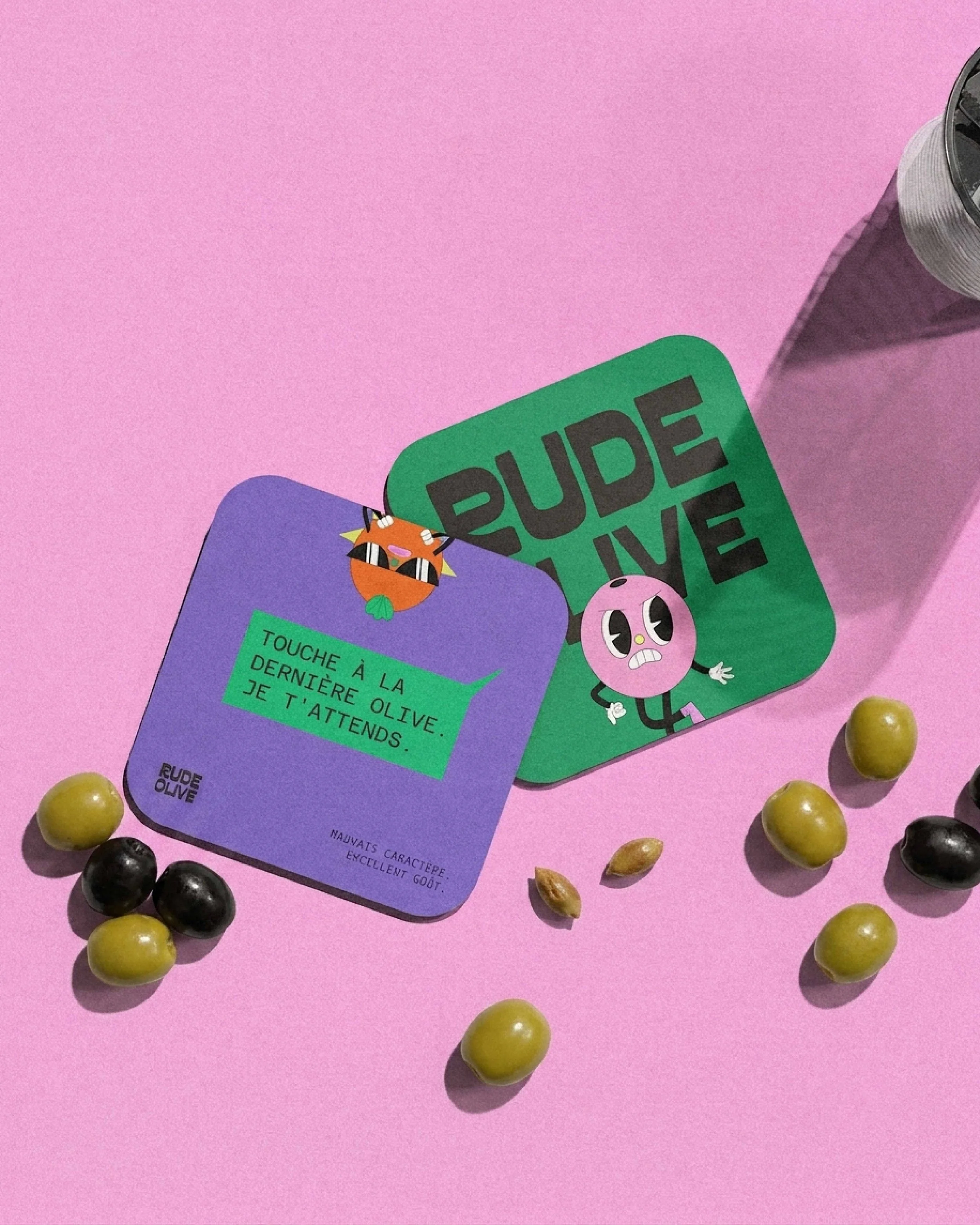 Deux boîtes de correcteur d'eczéma, une verte et une violette, entourées de plusieurs olives vertes et noires sur un fond rose.