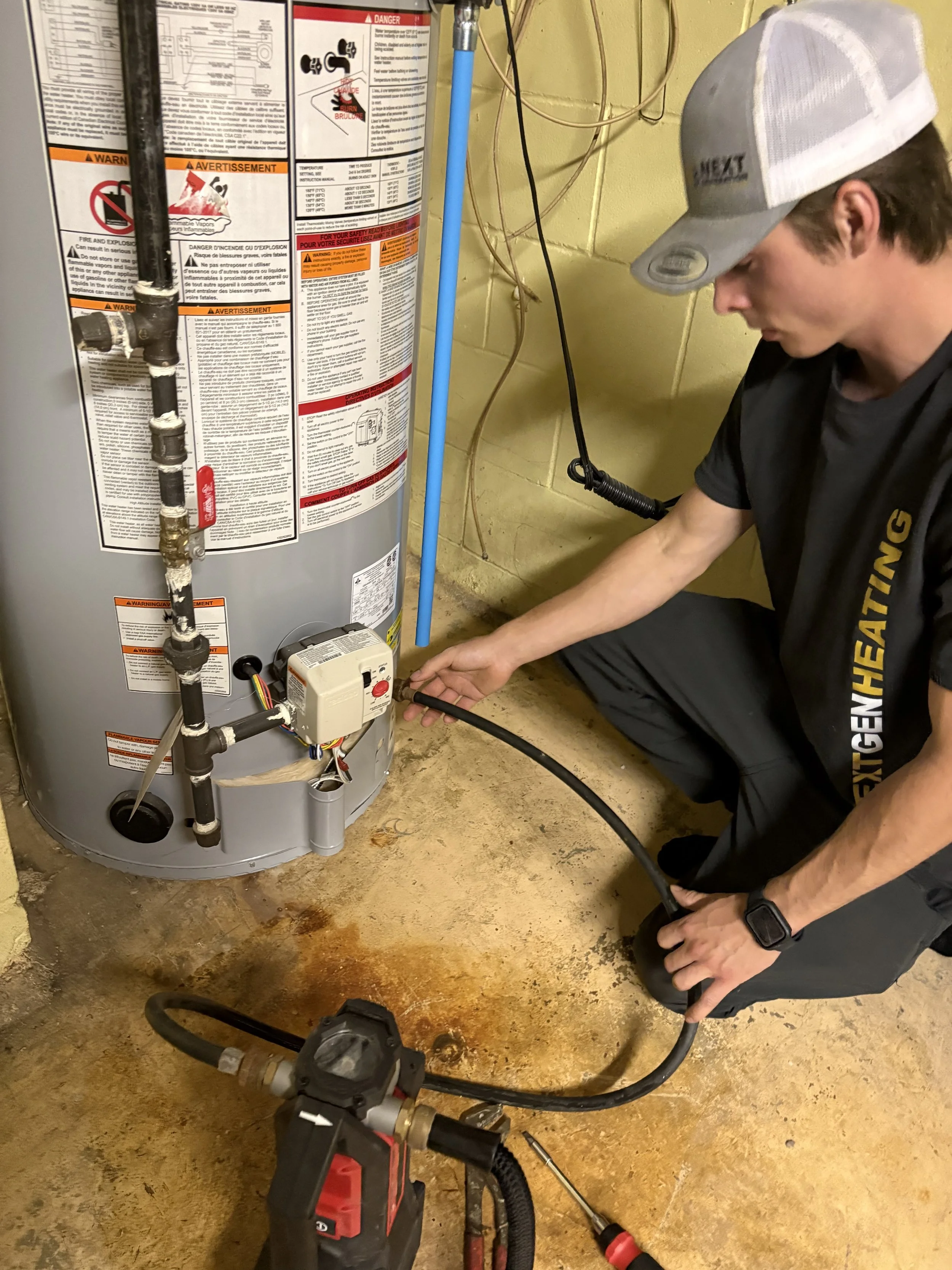 A technician in blue uniform and cap repairing a water heater, holding a red pipe wrench near the water heater controls.