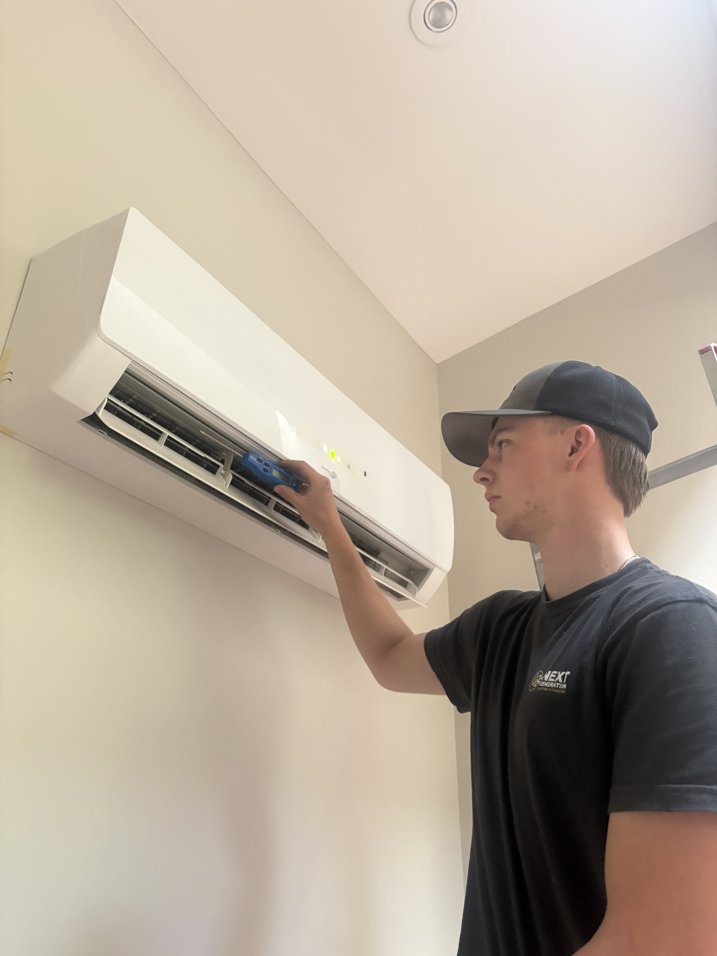 Technician fixing air conditioning unit outside a modern wooden house, kneeling on the grass with tools and equipment.