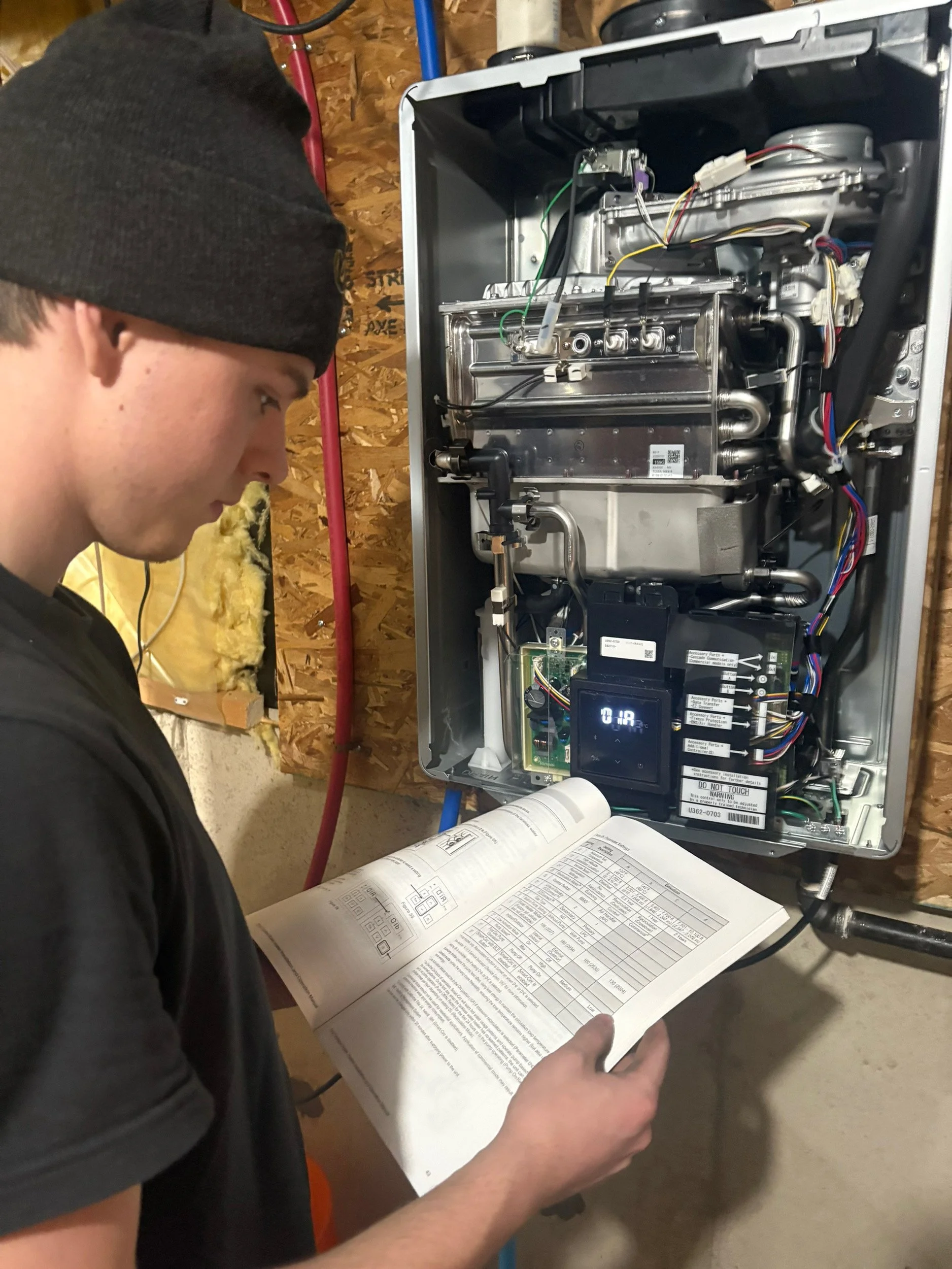 A technician with a watch on his left wrist is inspecting an open electrical control panel in a building utility room.