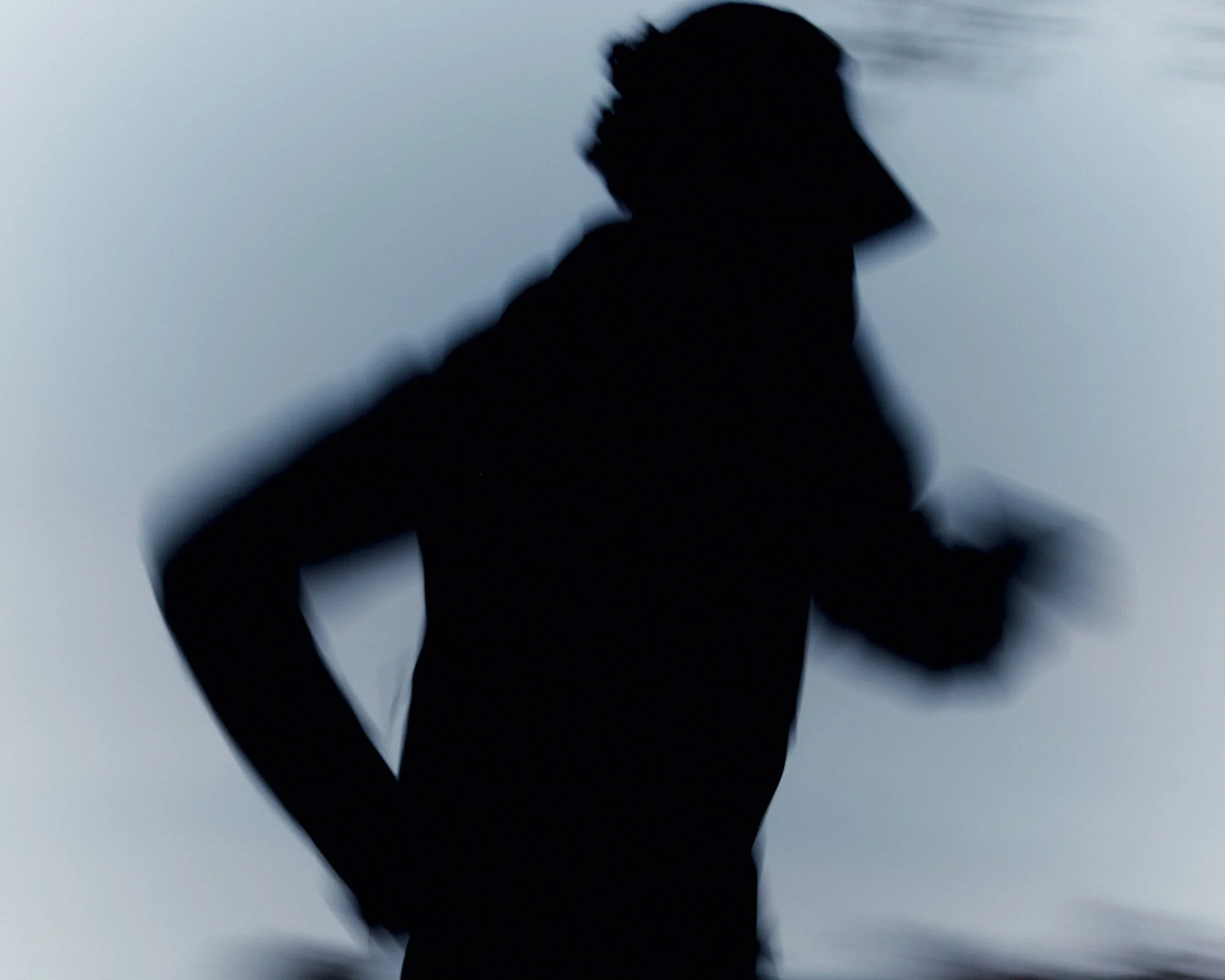Silhouette of a person with their hand on their head against a light background.