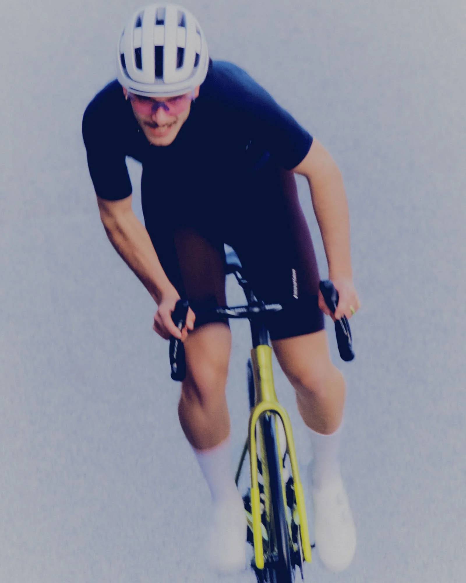 A person wearing a white bike helmet and pink sunglasses riding a yellow bicycle on a paved road.