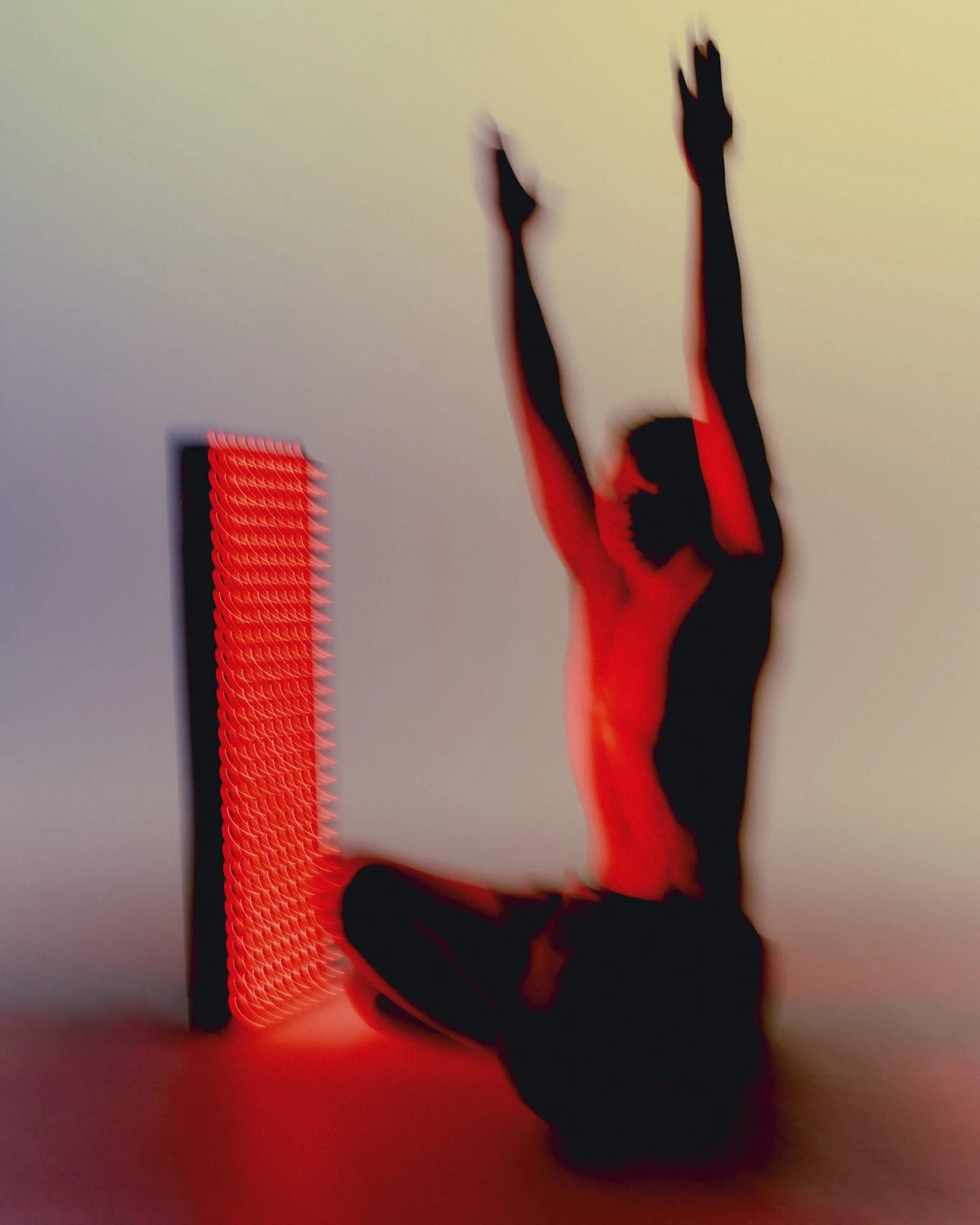 Silhouette of a man performing a yoga pose with her arms raised, illuminated by red lighting, with a patterned red light on the left side of the image.