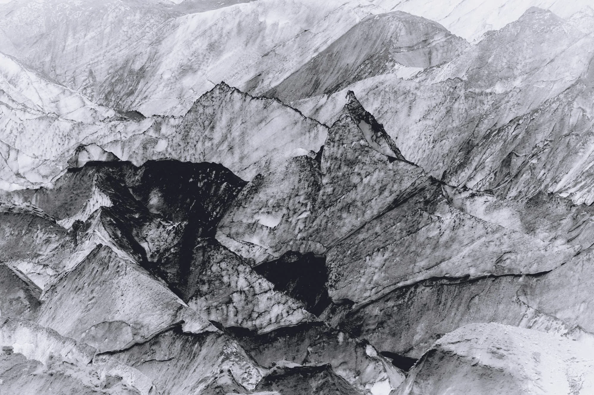 A black and white photograph of a rugged mountain range with sharp, jagged peaks and ridges.