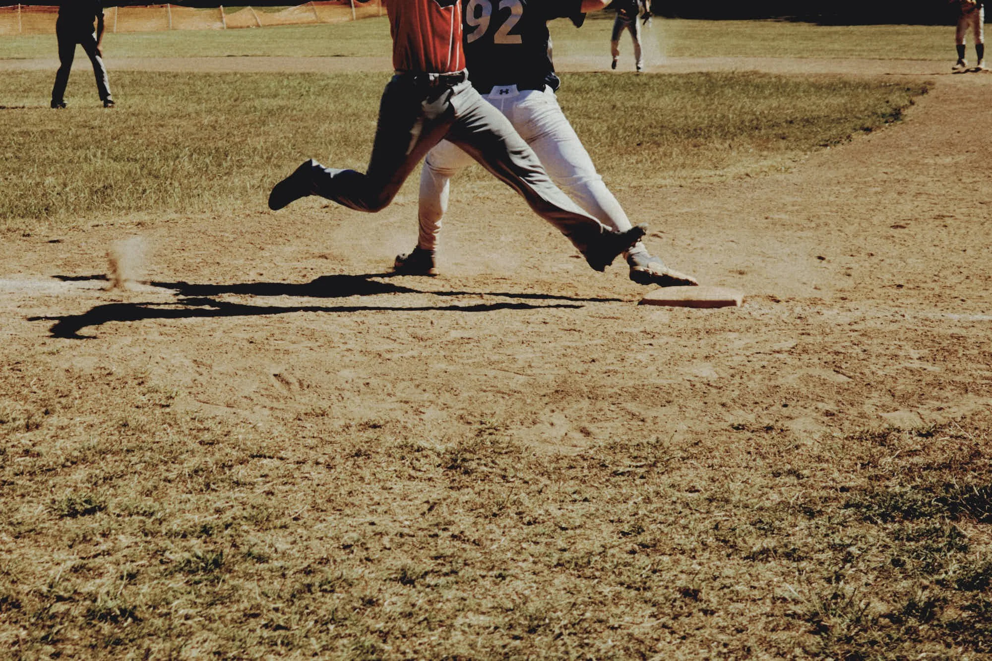 Two baseball players running on a dirt field, with other players in the background.