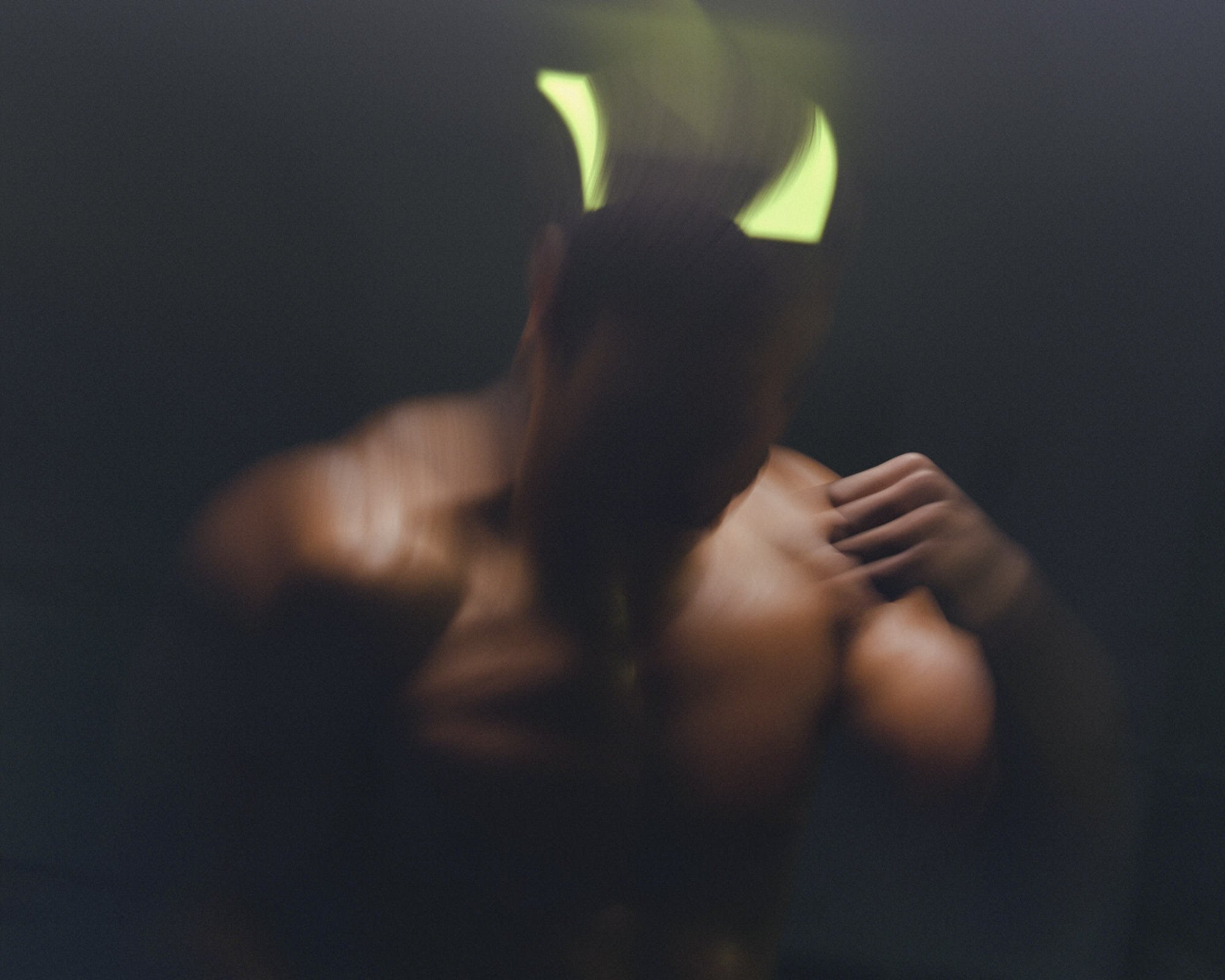 A close-up image of a blond person with short hair, seen from behind, holding a glow-in-the-dark triangular object