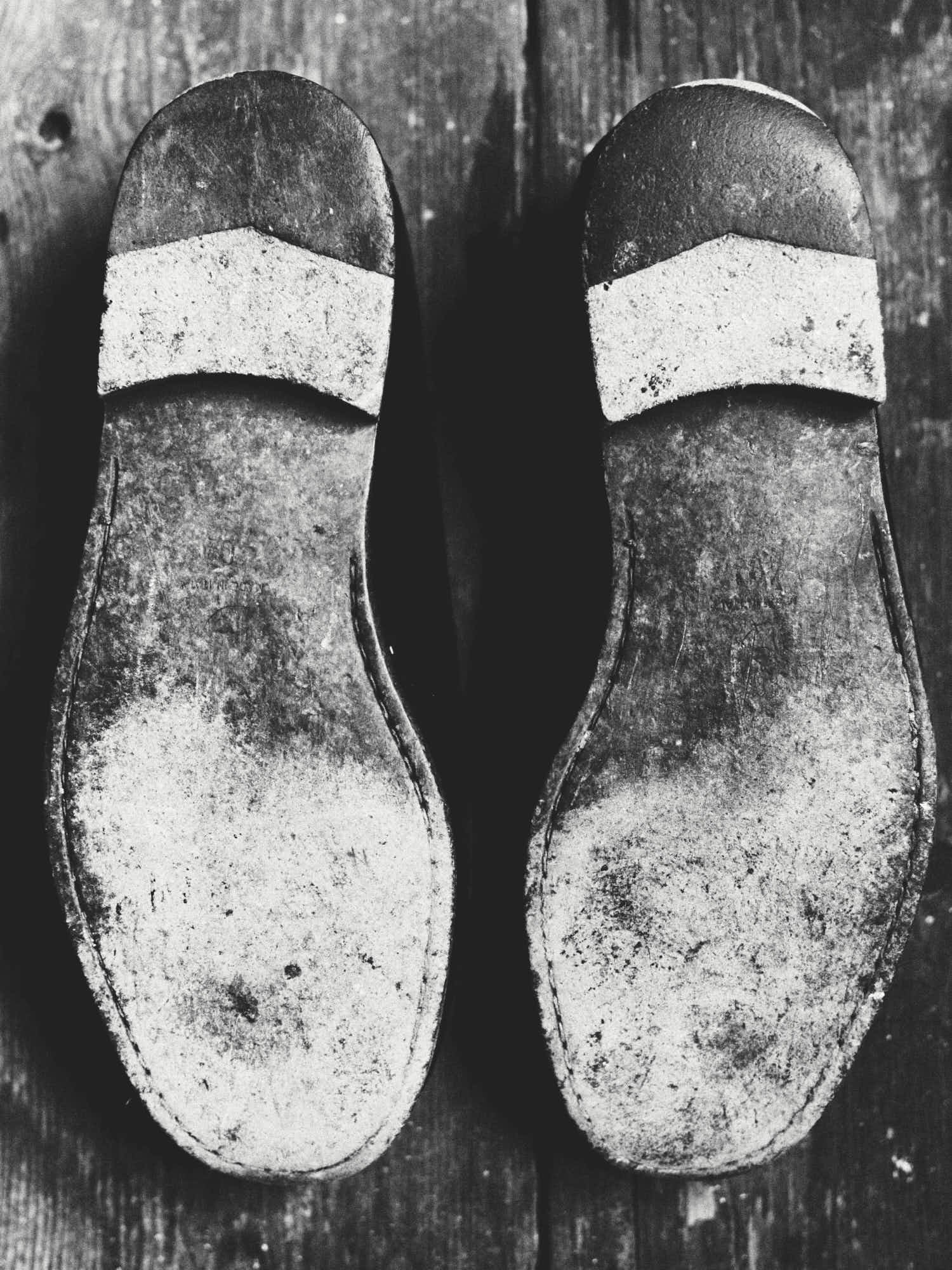 Top view of two worn-out shoes with painted toe caps resting on a wooden surface.