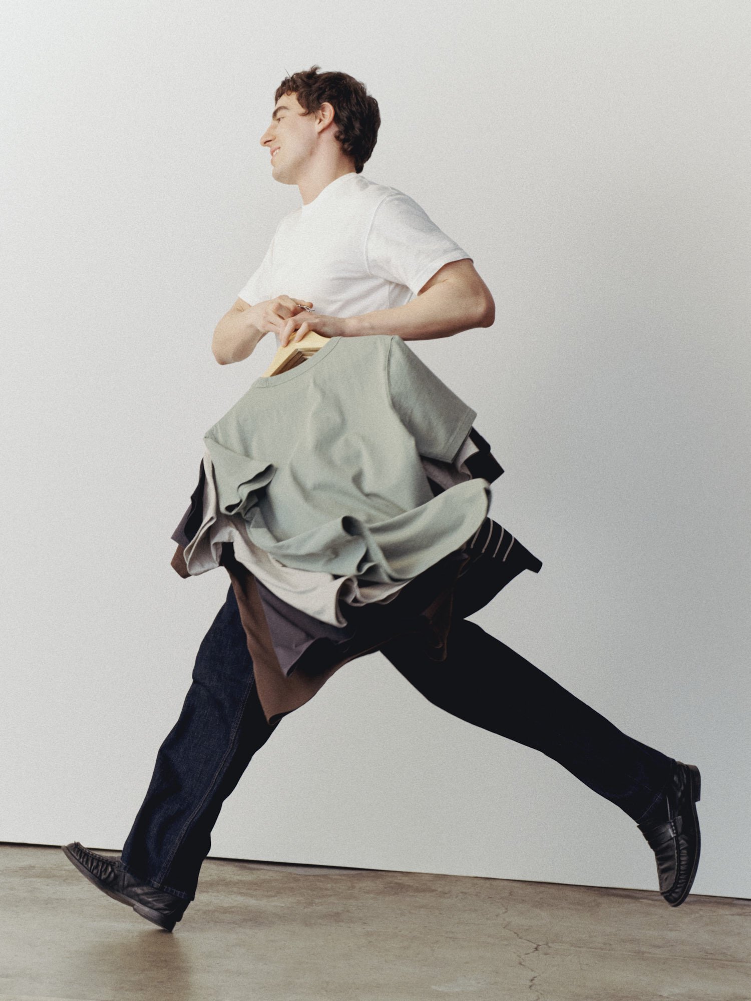 A person running with a large bag filled with clothes, wearing a white t-shirt and black boots, against a plain background.