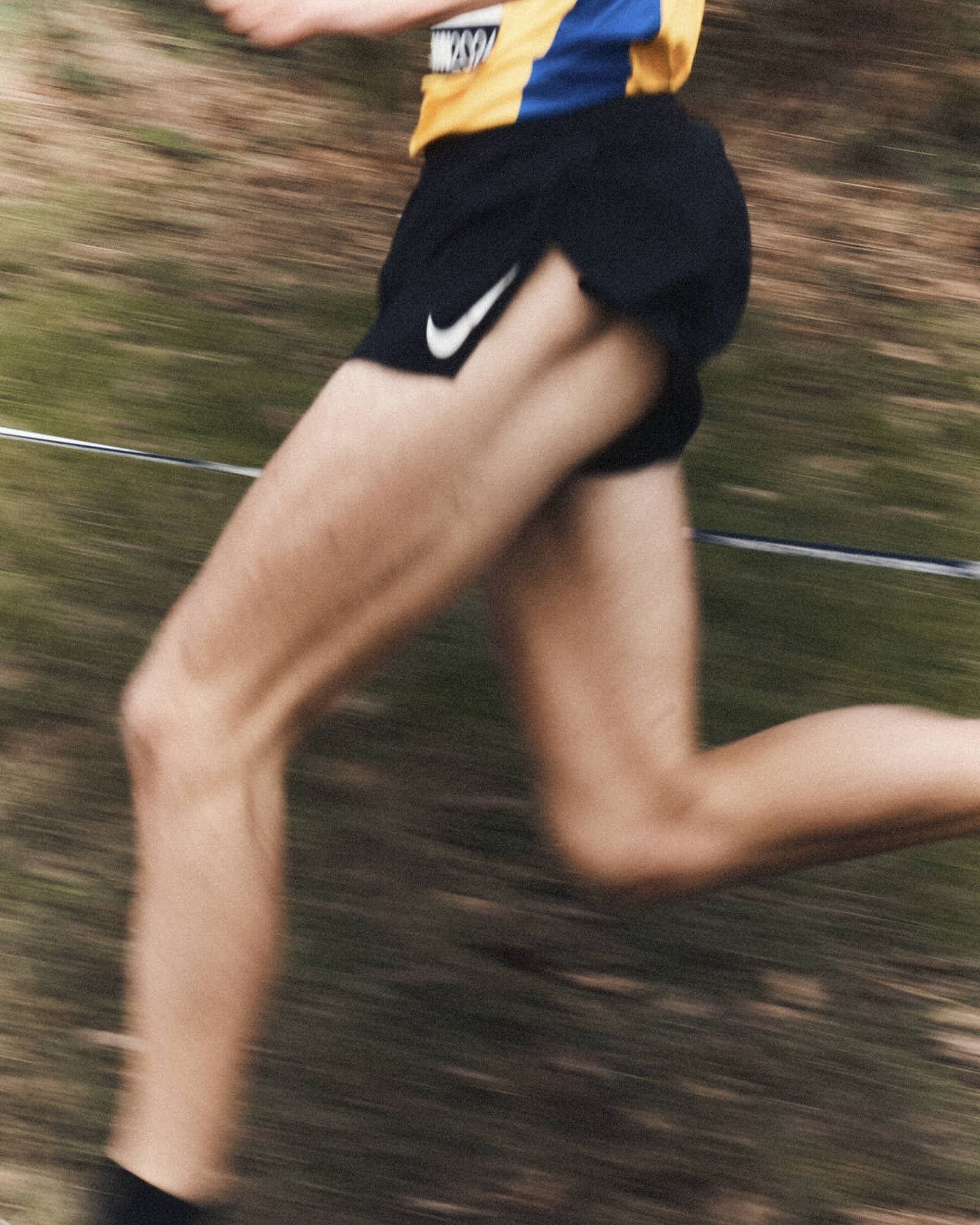 A person running outdoors, wearing black shorts with a Nike logo and a multicolored shirt. The image is blurred, indicating motion.