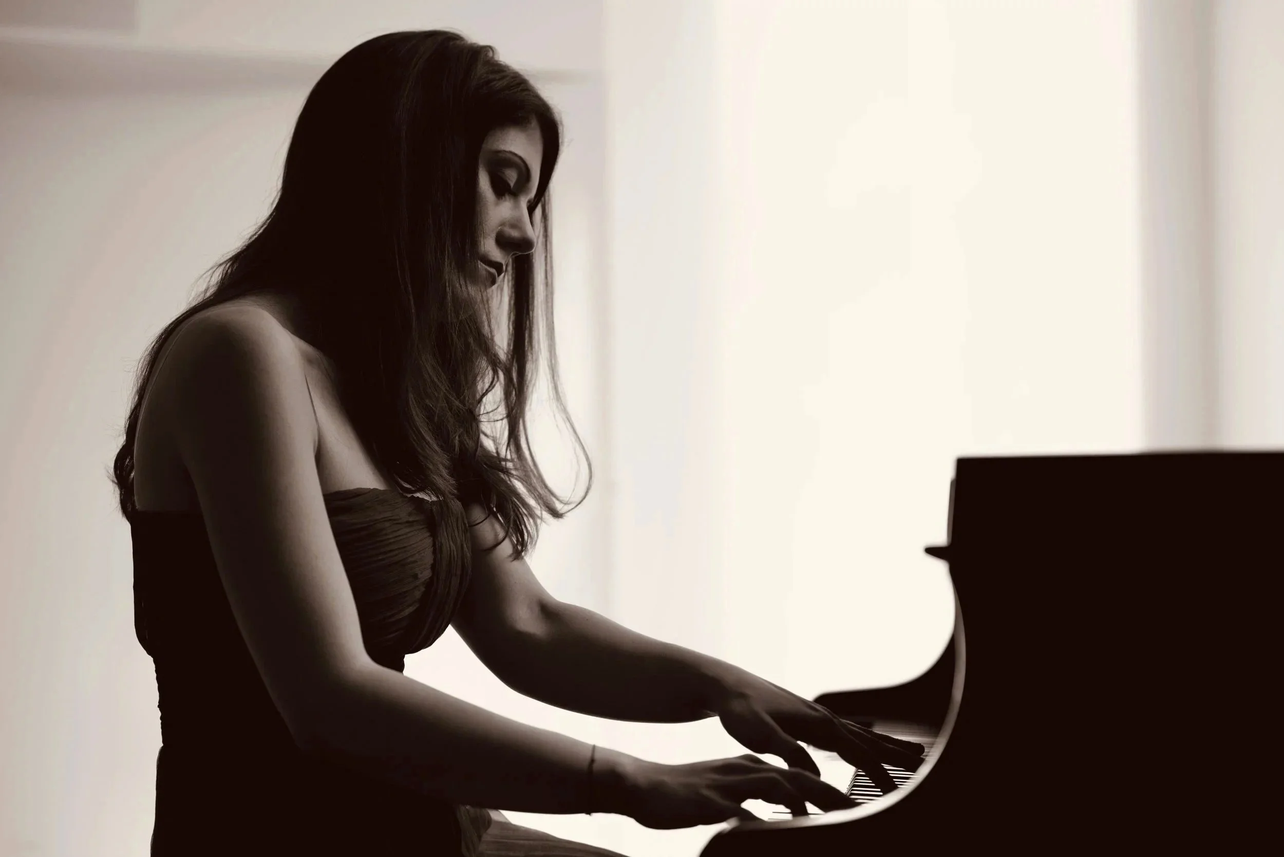Woman playing piano in soft lighting, silhouette with focused expression.