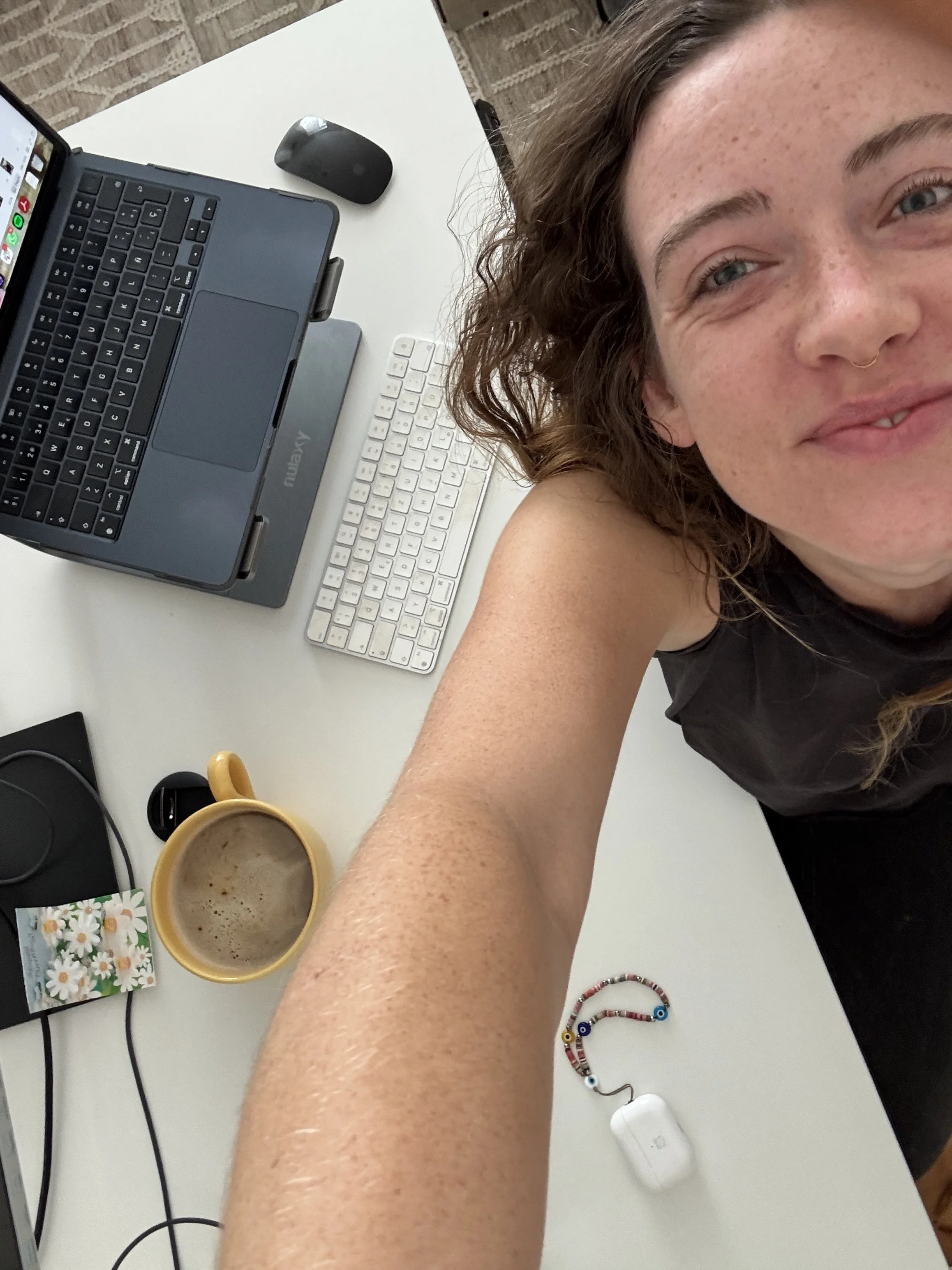 A person taking a selfie at a desk with a laptop, keyboard, mouse, and coffee mug, with accessories and a computer mouse visible on the desk.
