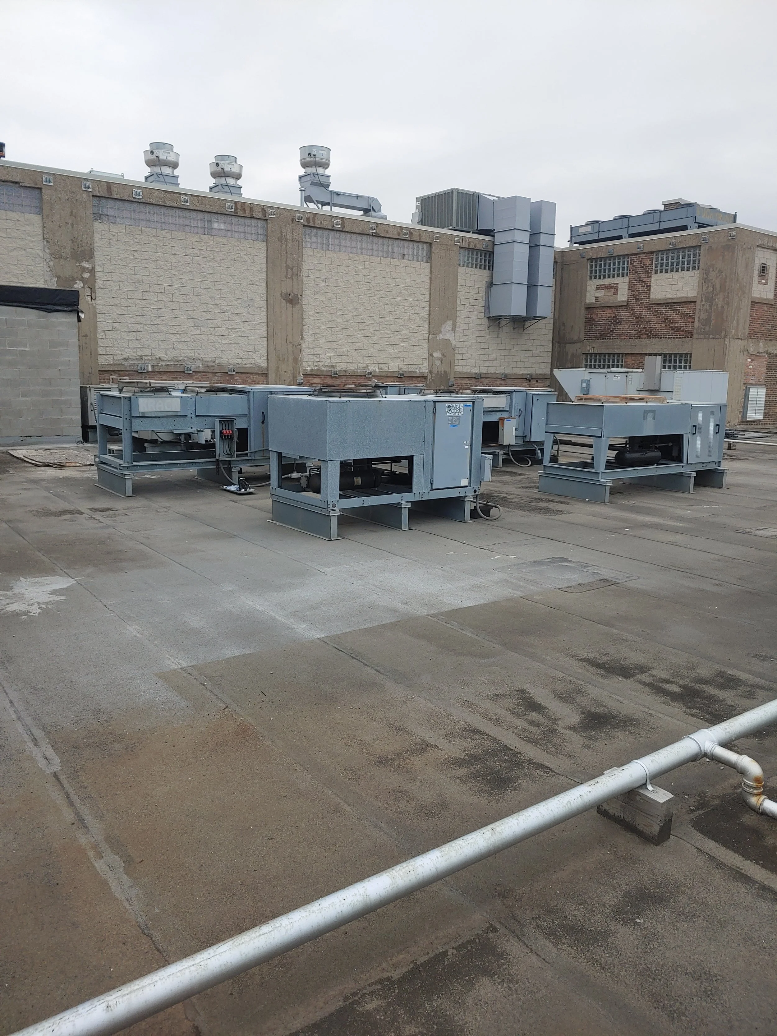 Roof top with HVAC units and exhaust fans on a commercial building, cloudy sky, concrete surface with pipe barrier.
