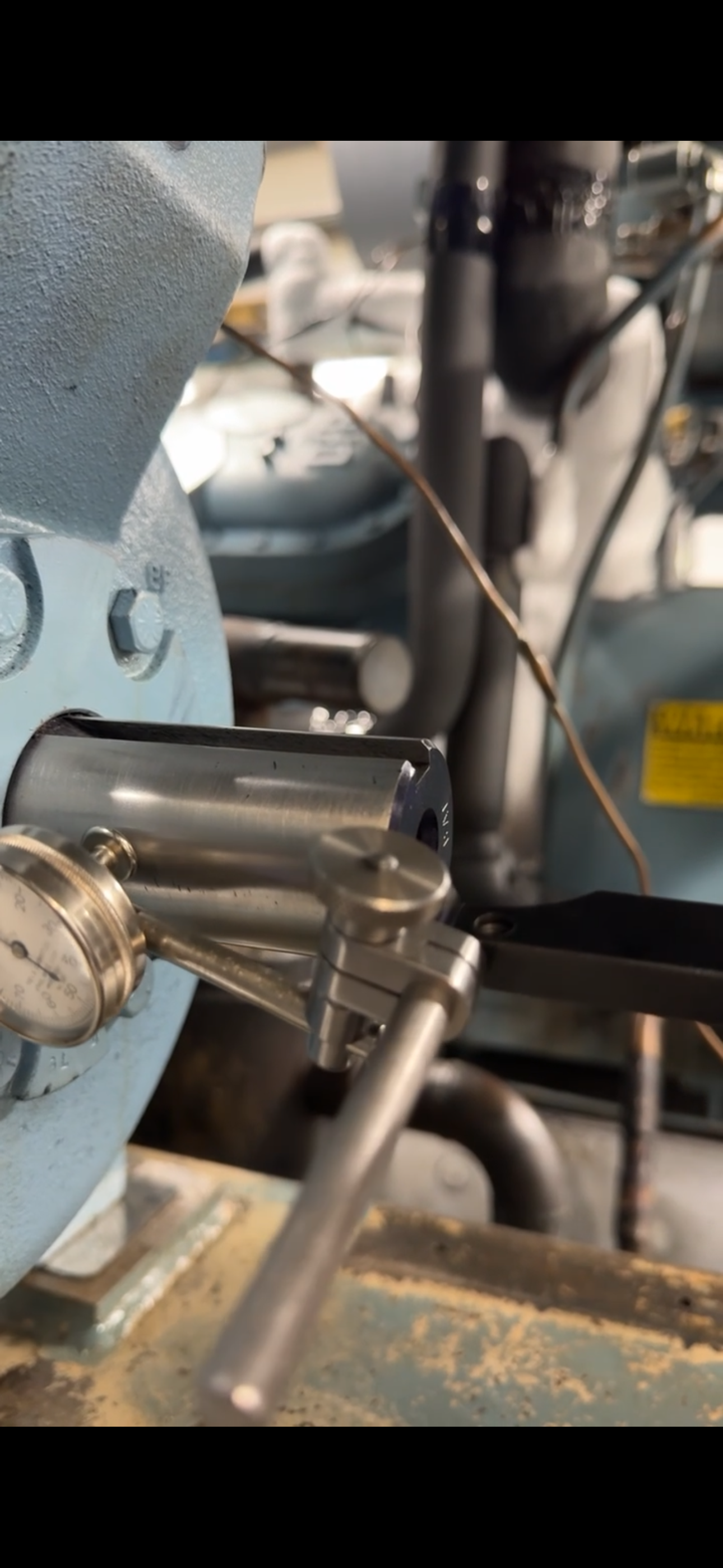 Close-up of a metal industrial machine with gauges, levers, and a copper wire connected to it.