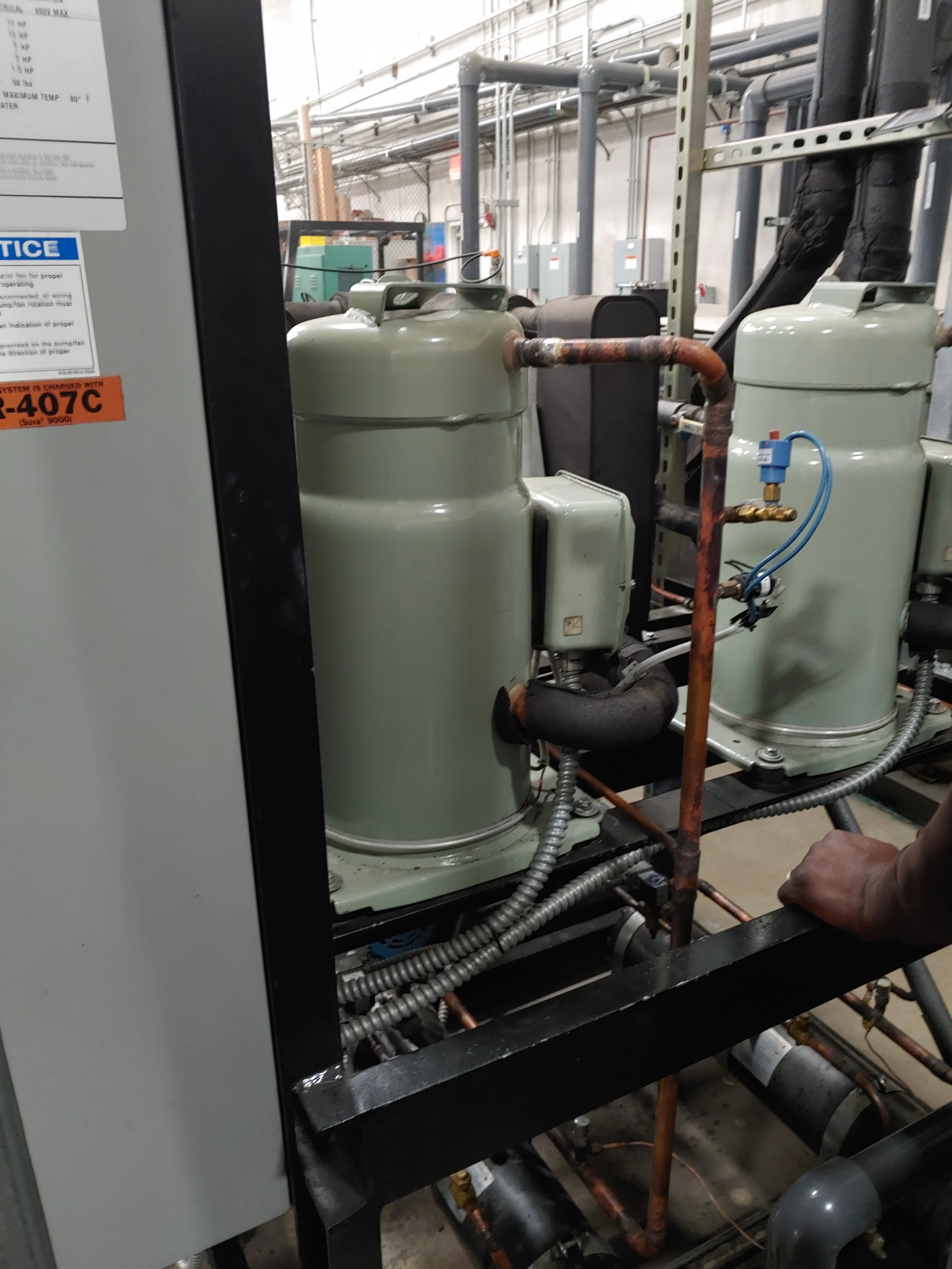 Industrial refrigeration compressor unit with copper pipes, electrical components, and control systems in a utility room.