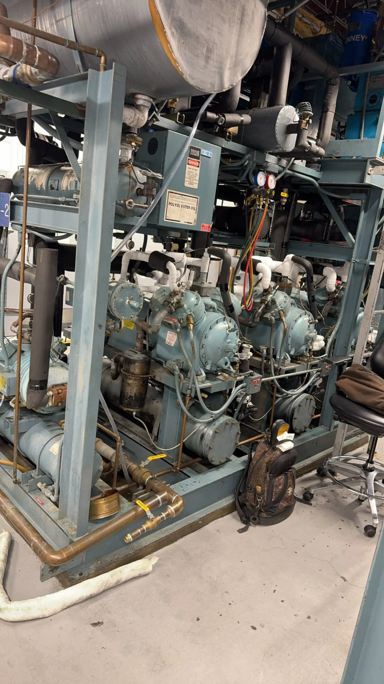 Industrial refrigeration or HVAC equipment with pipes, valves, gauges, and compressors in a mechanical room.