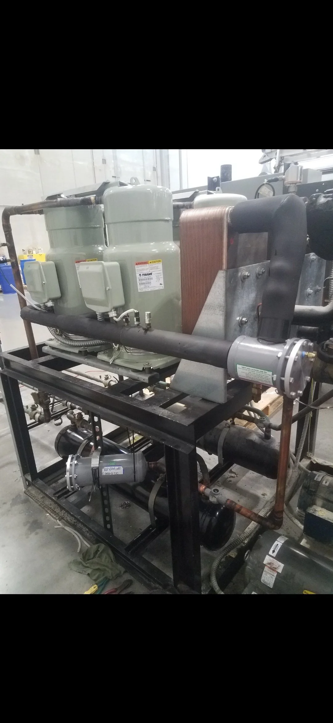 Industrial chiller system with compressors, pipes, and tubing mounted on a black metal frame.