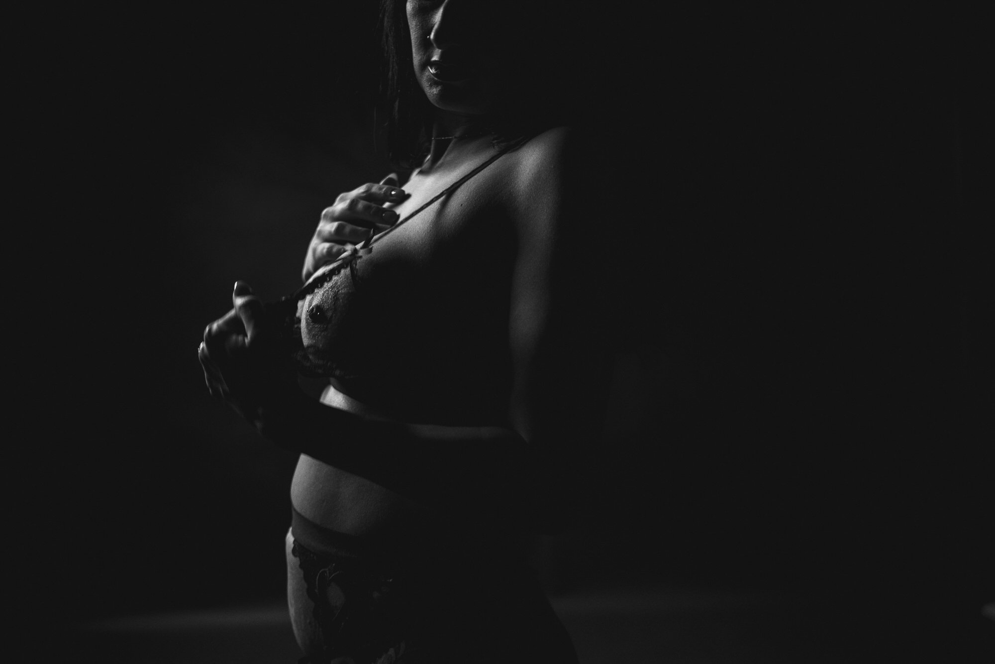 A black and white photograph of a woman in lingerie, partially in shadow, with her hand on her chest.