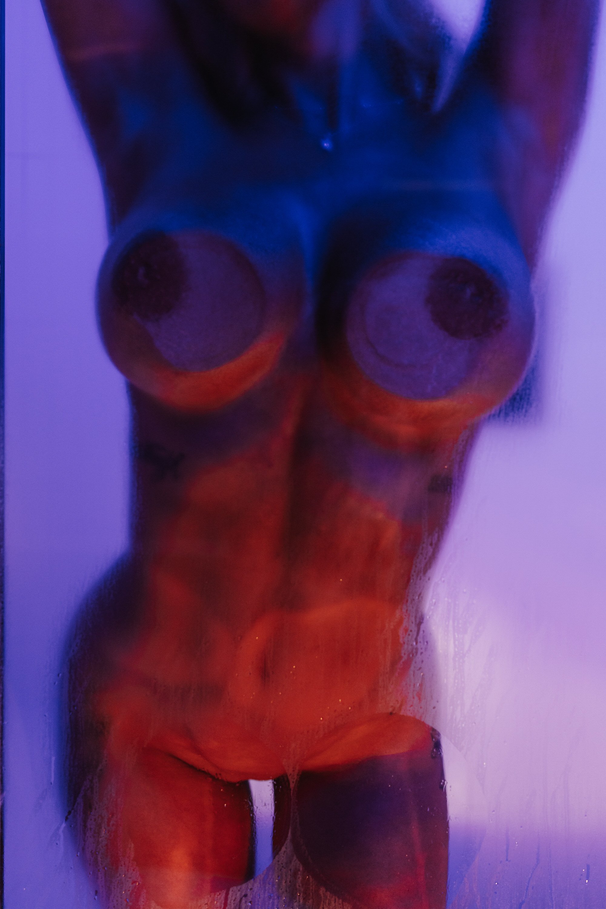 A person kneeling with their back to the camera, illuminated by purple and red lighting, with their buttocks and lower back exposed.