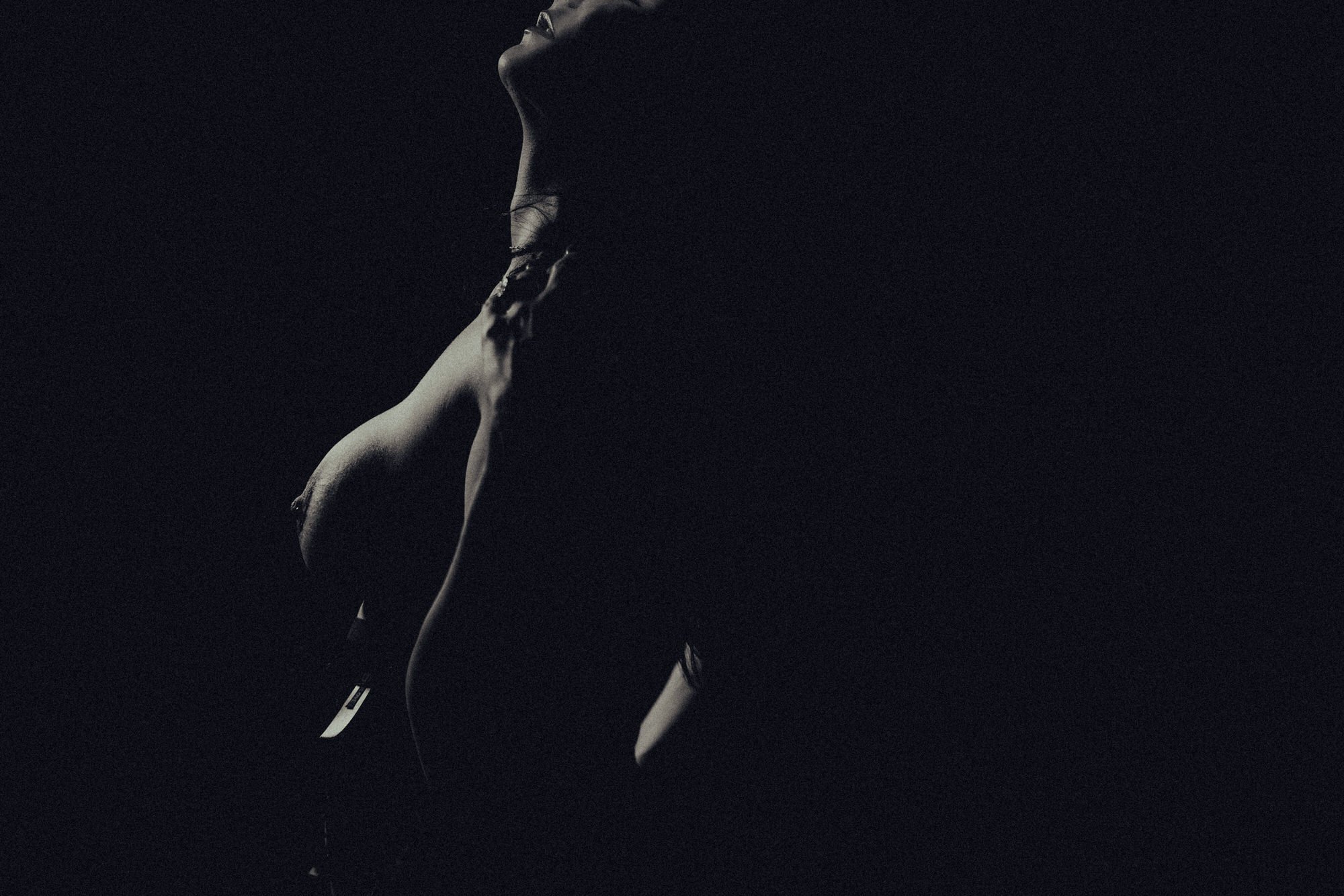 A black and white photo of a person's silhouette with their head tilted back, delicate facial features, and long hair falling over their shoulders, against a dark background.