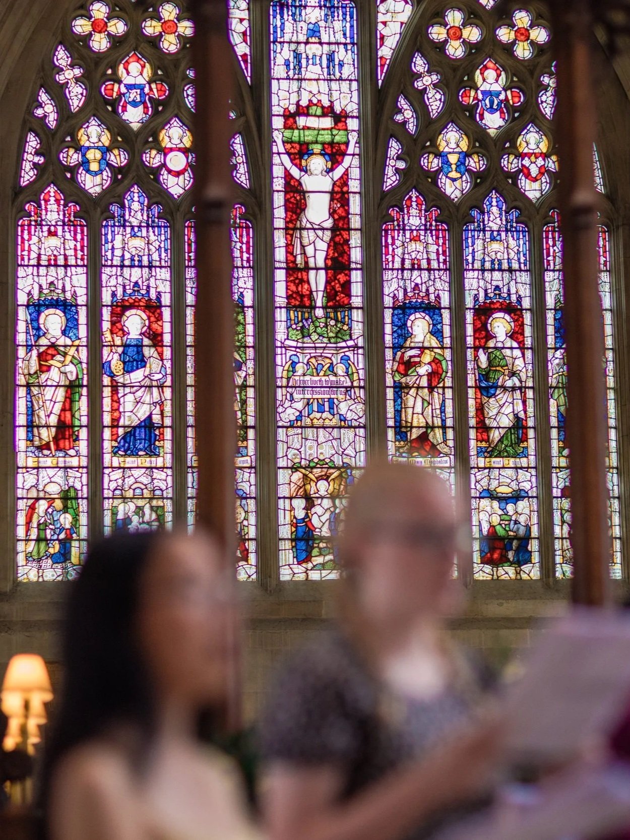 Colorful stained glass church window depicting religious figures, including Jesus on the cross, saints, and angels.