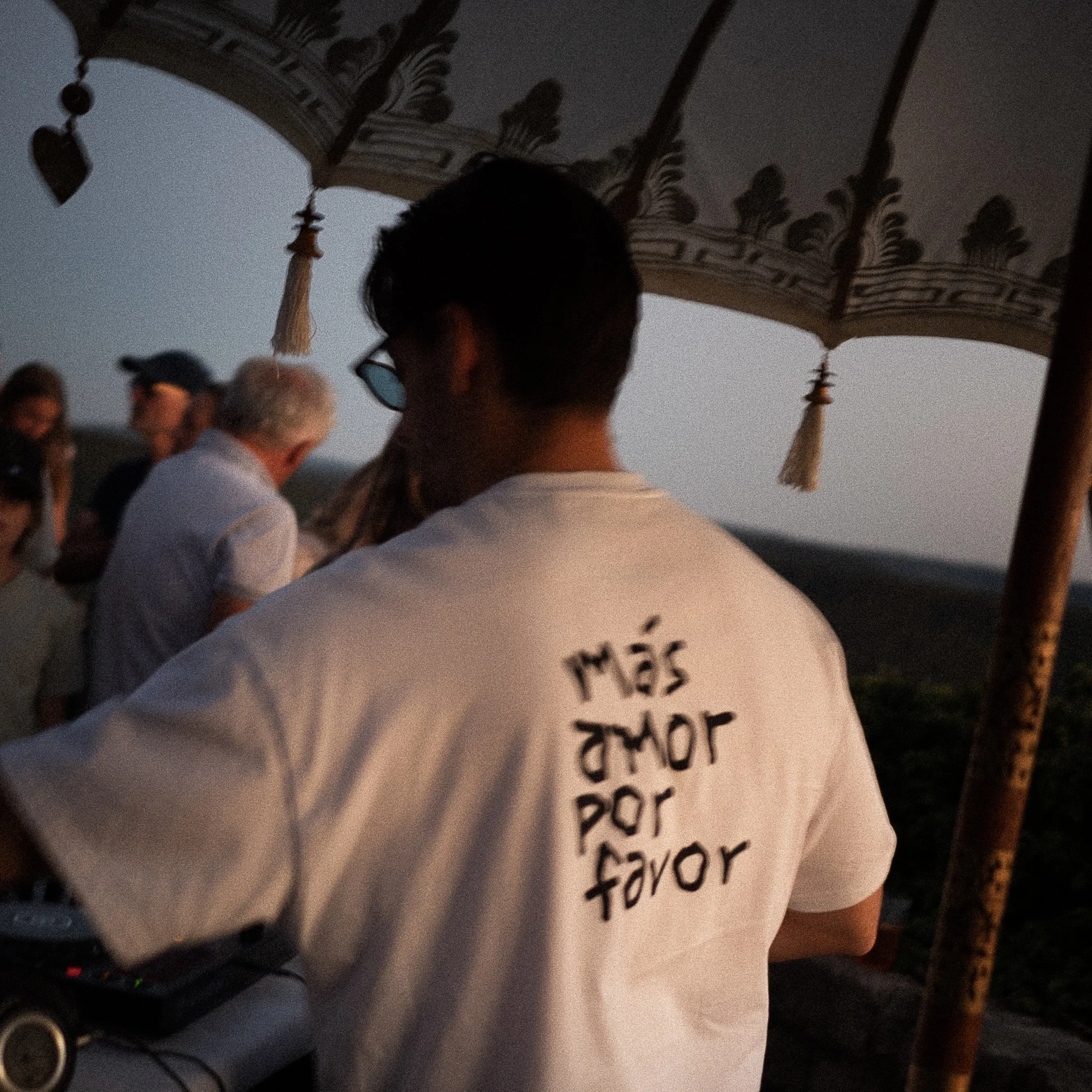 Menschen stehen im Kreis mit einem großen weißen Schild mit lateinischer Schrift, unter einem dekorativen Dach bei Sonnenuntergang.