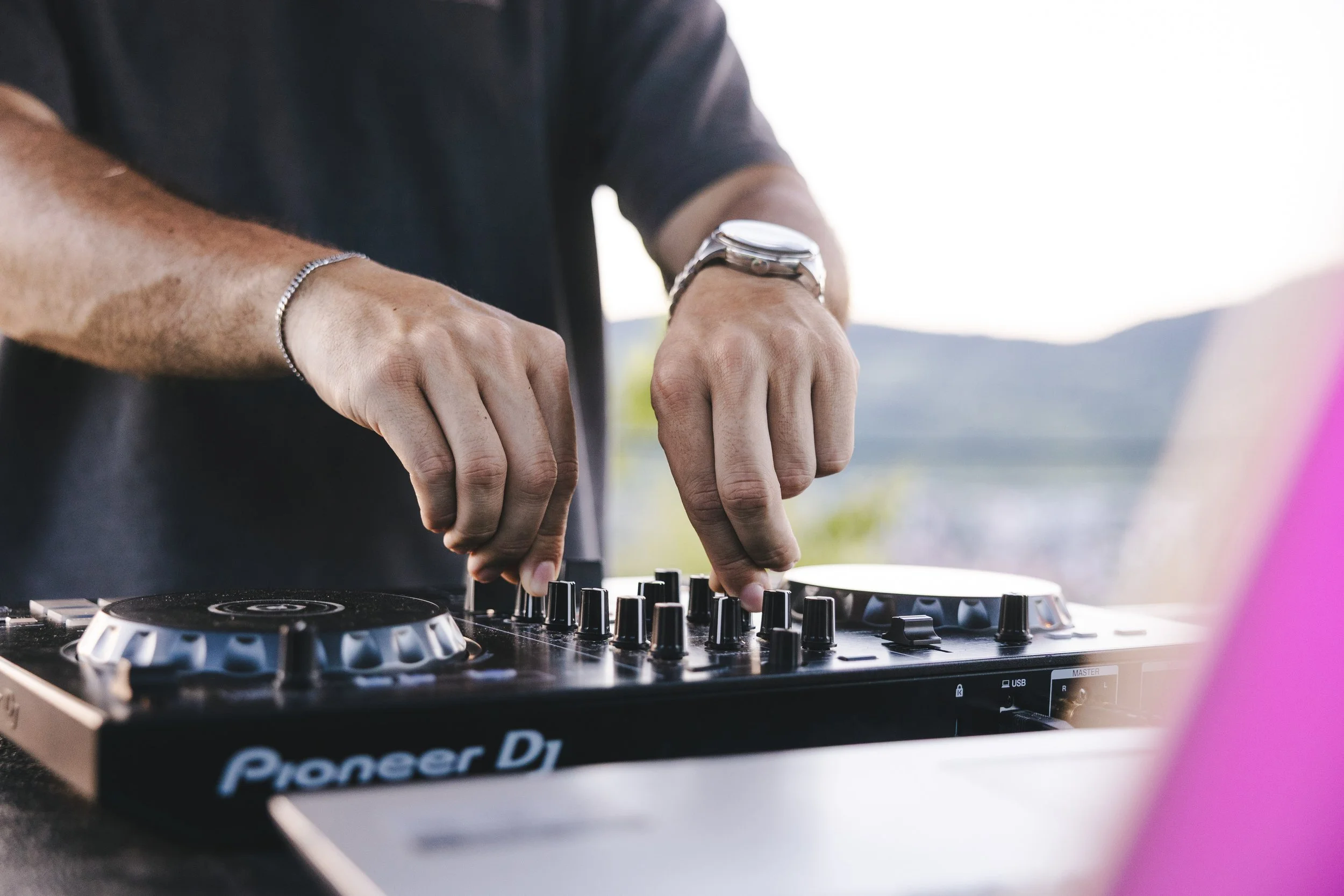 Nahaufnahme eines wellengeschwungenen Kopfes und einer Person, die an einem DJ-Controller mit den Marken Pioneer DJ arbeitet, mit einem natürlichen, verschwommenen Hintergrund im Freien.