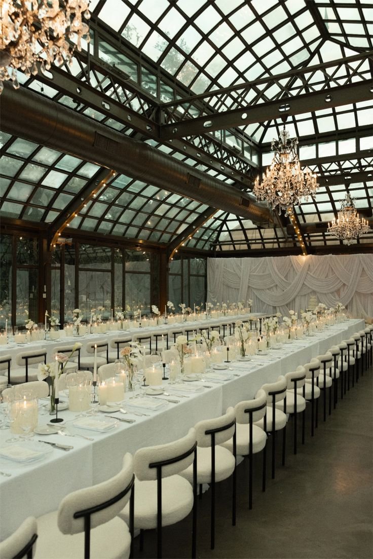 Eleganter festlich gedeckter Tisch in einem Glasschloss mit Kronleuchtern, Tafel mit weißen Laken, Kerzen, Blumen und Geschirr.
