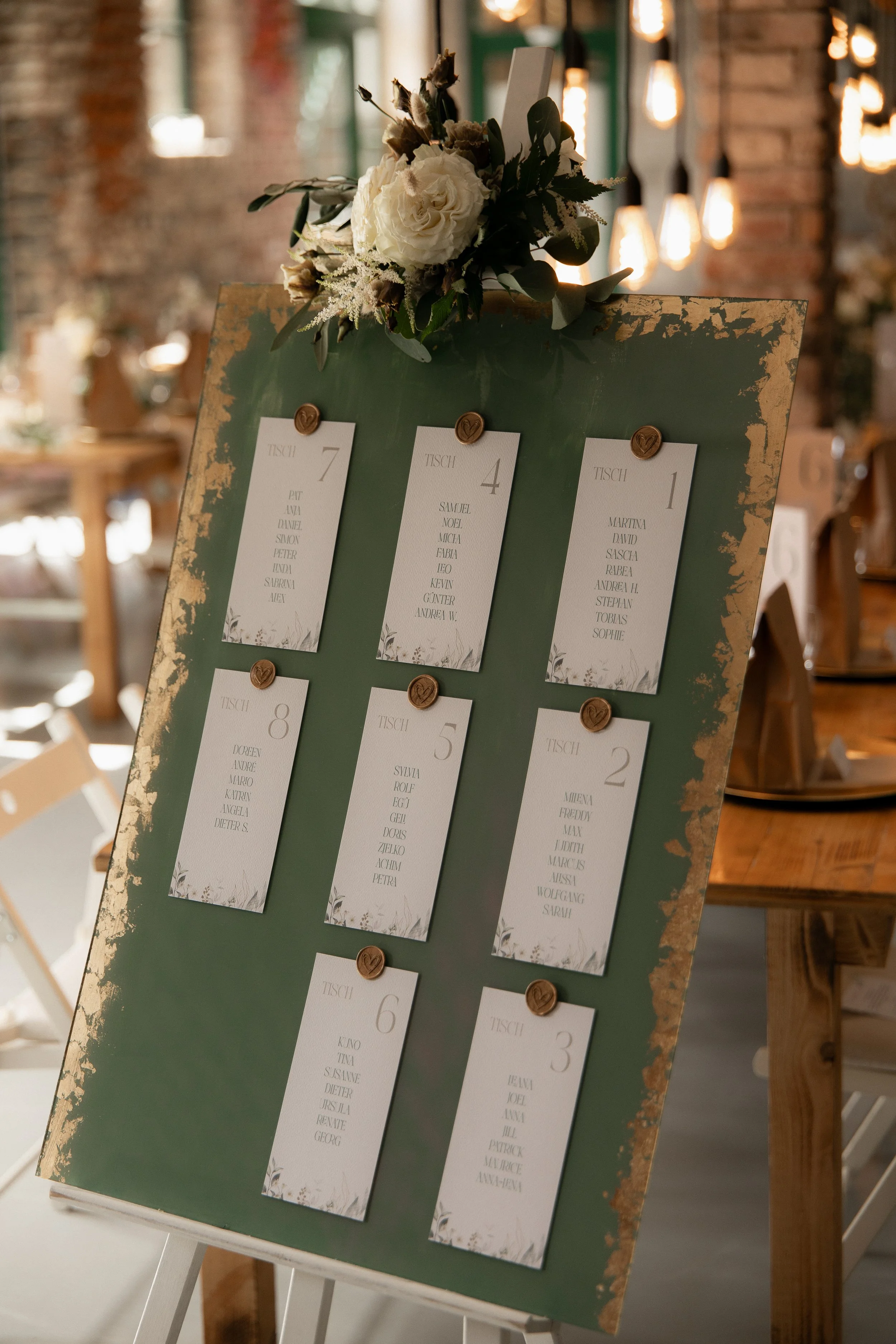 Grüner Hochzeitssitzplan auf Staffelei mit Namenskarten und Blumendekoration