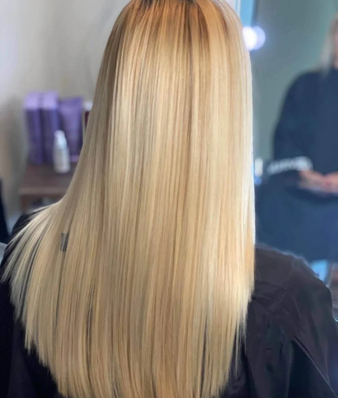 Back view of a woman with long, straight, blonde hair seated in a salon.