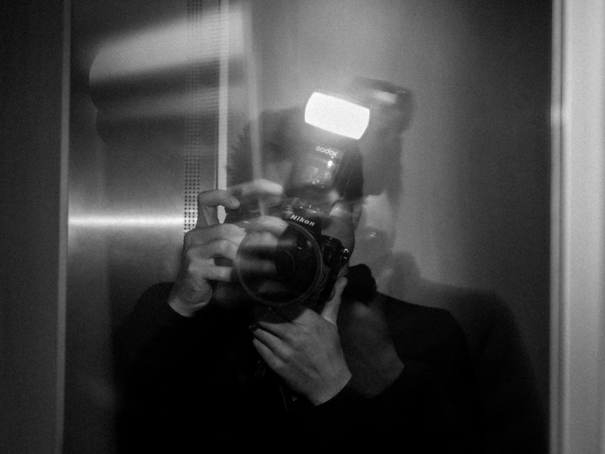 Reflet d'une personne prenant une photo avec un appareil photo numérique dans un ascenseur, avec une main visible tenant l'appareil et un écran lumineux.