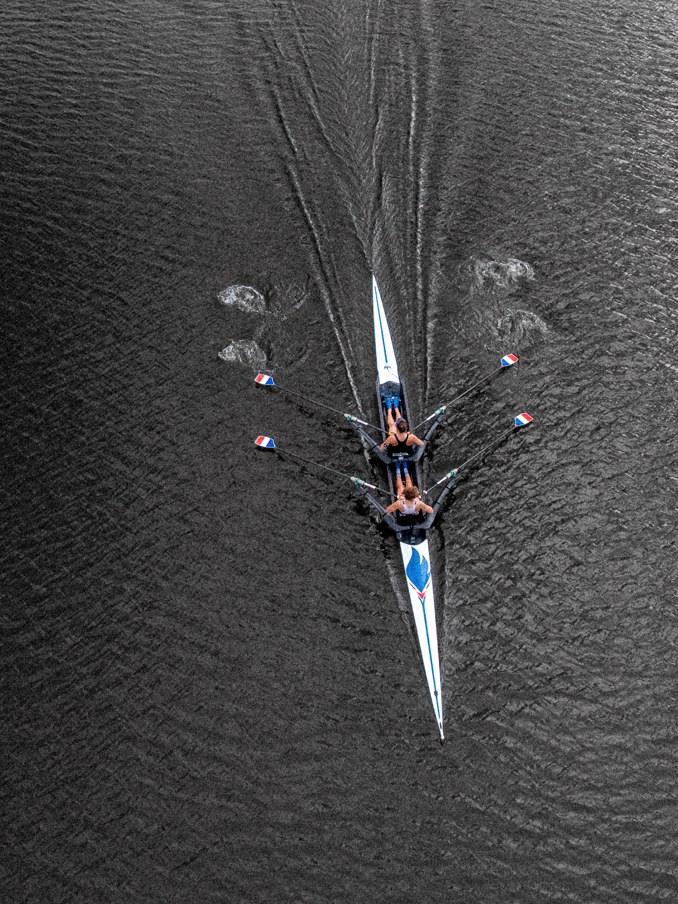 Une rame de kayak à pagaie dans l'eau sombre, vue d'en haut, avec deux personnes à bord.