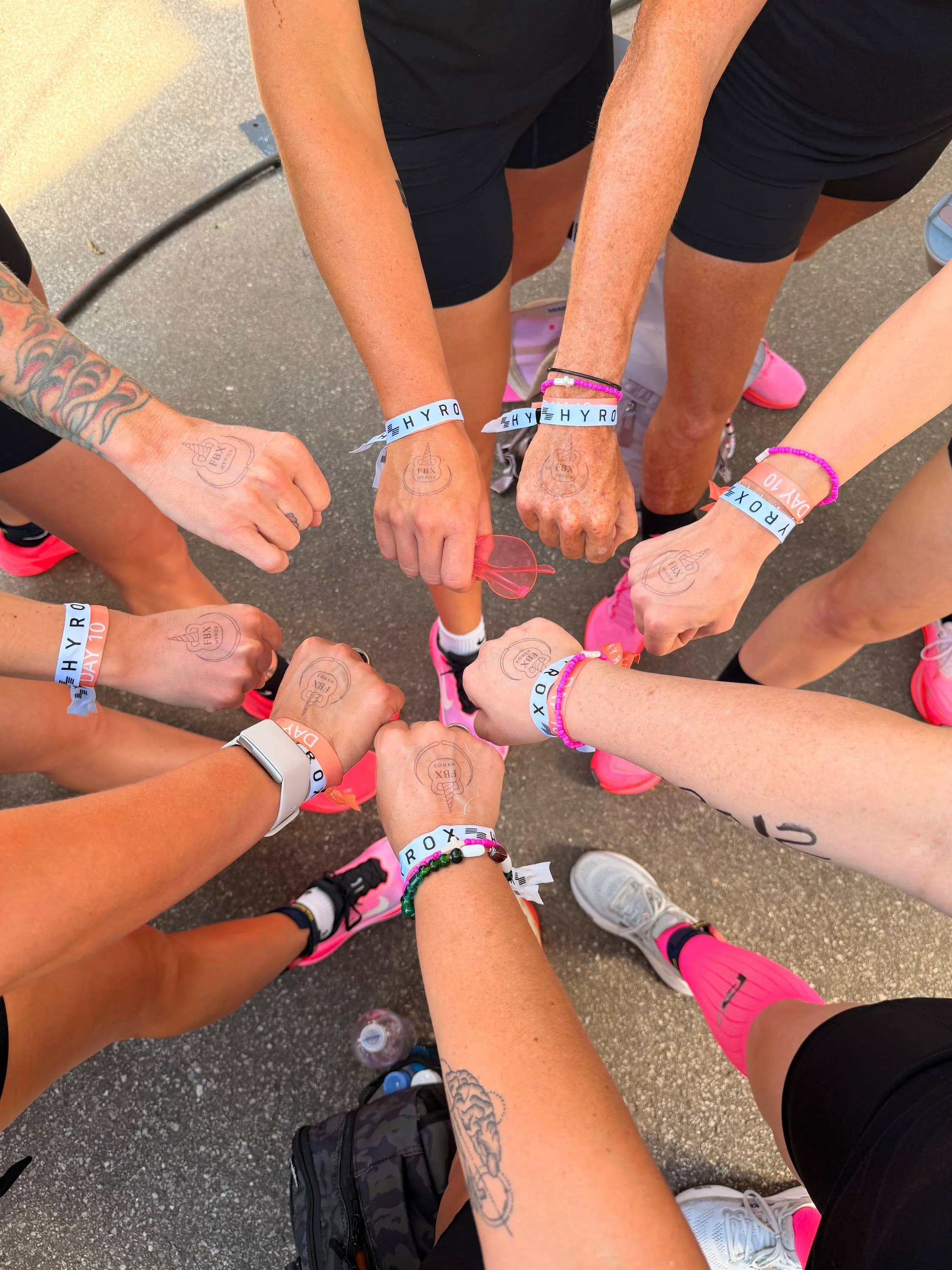 Multiple people forming a circle with their fists raised together, wearing pink running shoes, black shorts, and wristbands.
