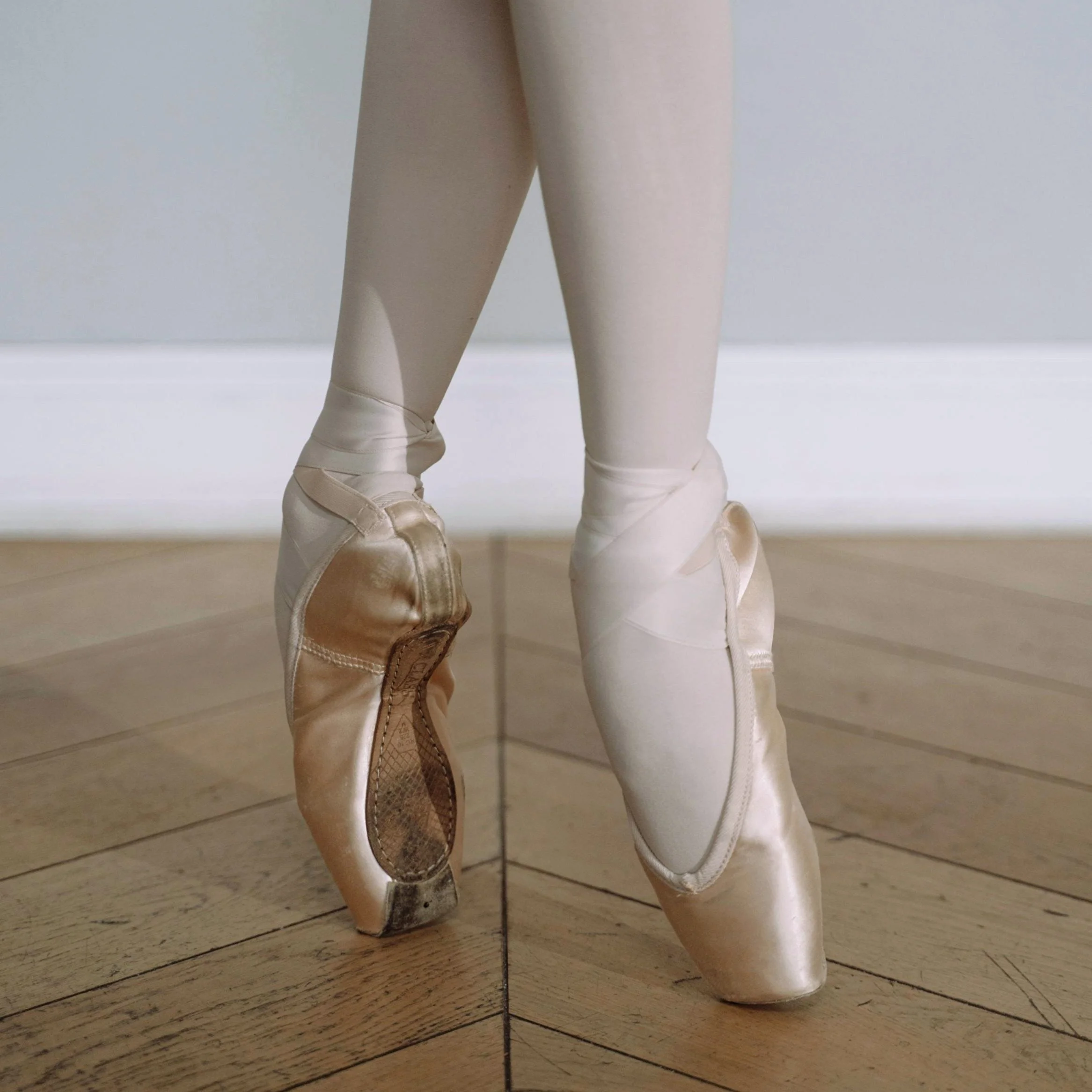 Pointes de ballet usées posées sur un parquet en bois.