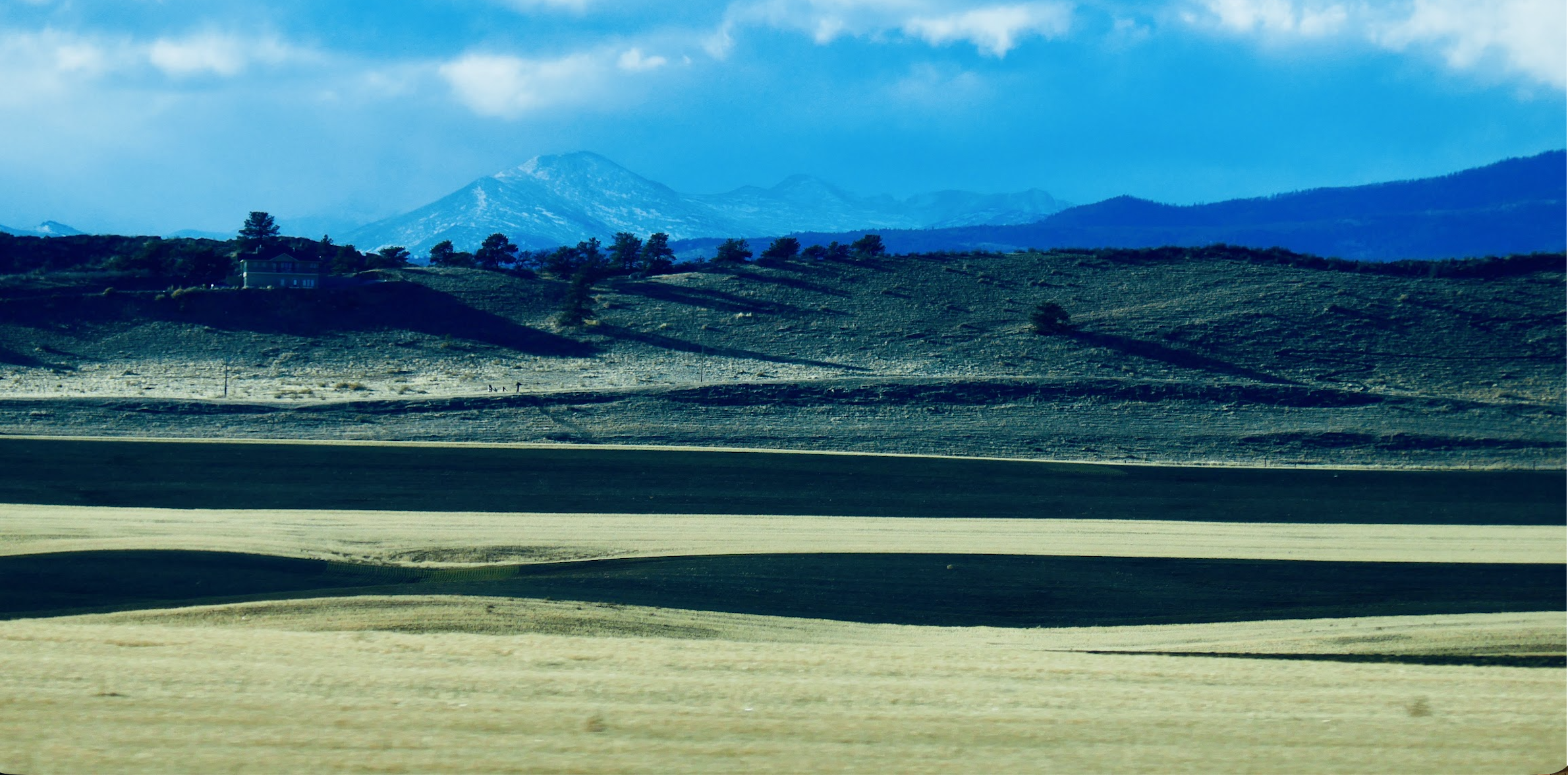 Layered fields, ridges and mountains beneath blue sky