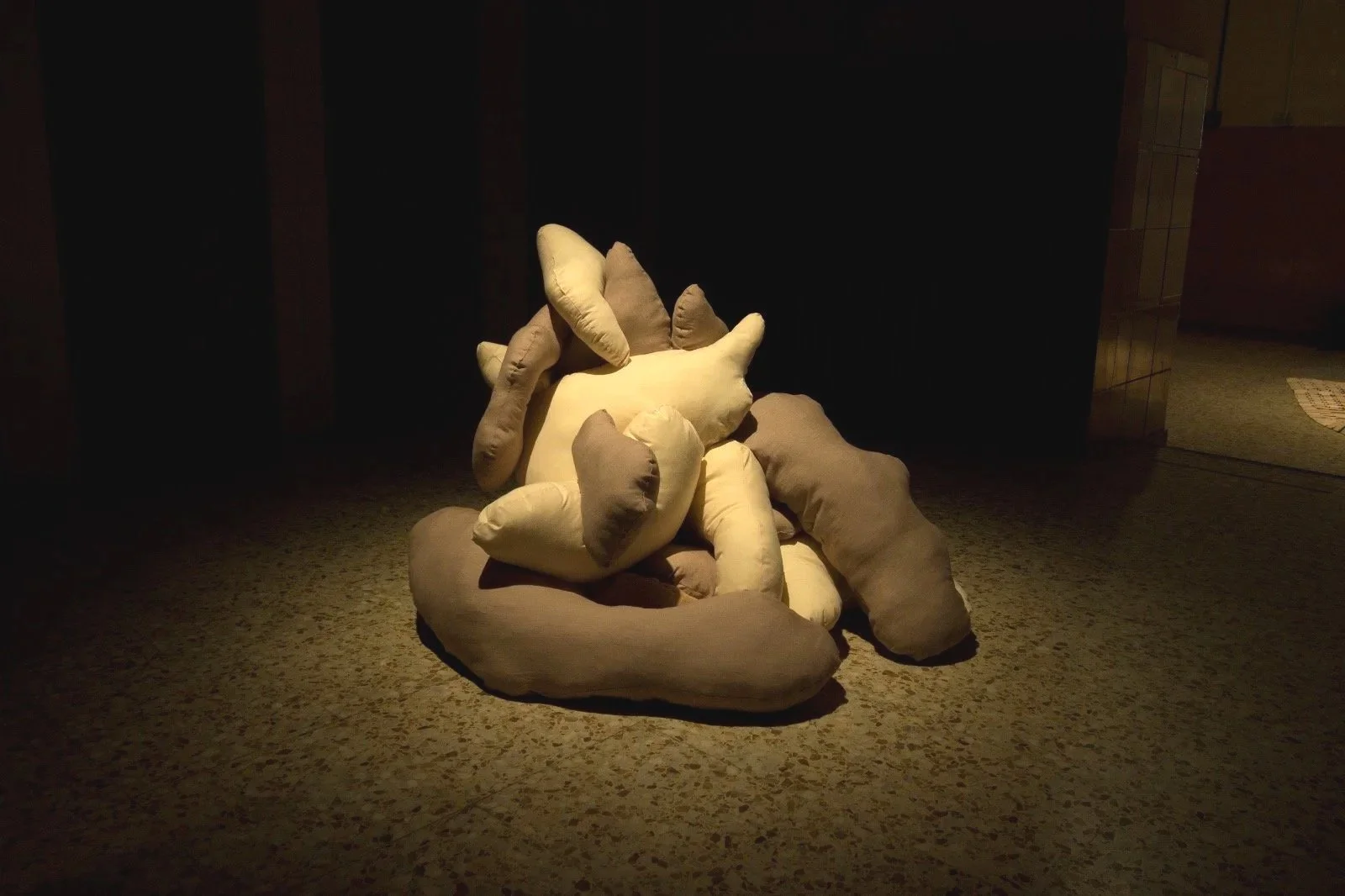 A cluster of plush, beige and brown stuffed animal shapes on a dimly lit carpeted floor
