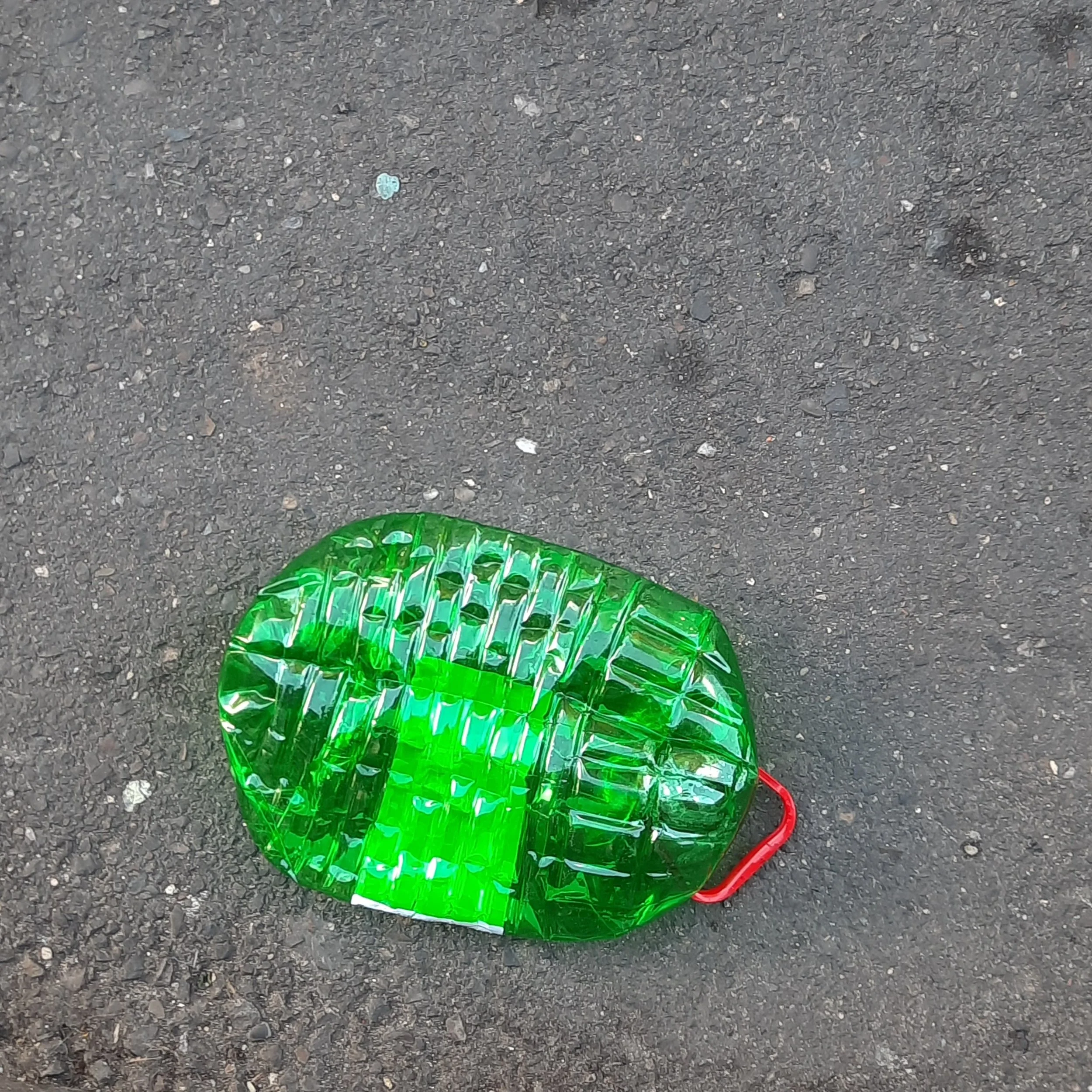 Green inflated balloon with a shiny surface on a rough asphalt ground. Part of a red string is visible at the bottom of the balloon.