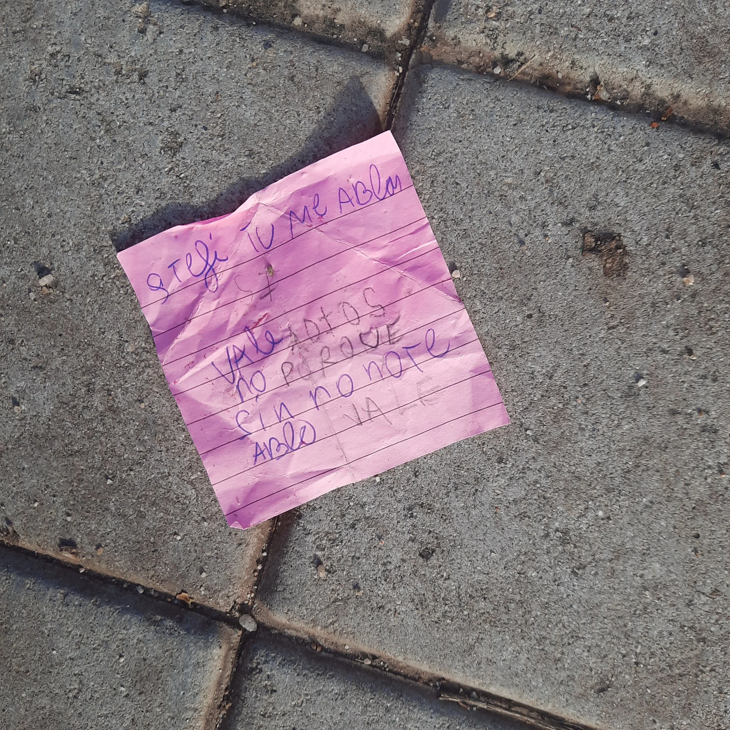 A crumpled pink piece of paper with handwritten text lying on a rough concrete surface.