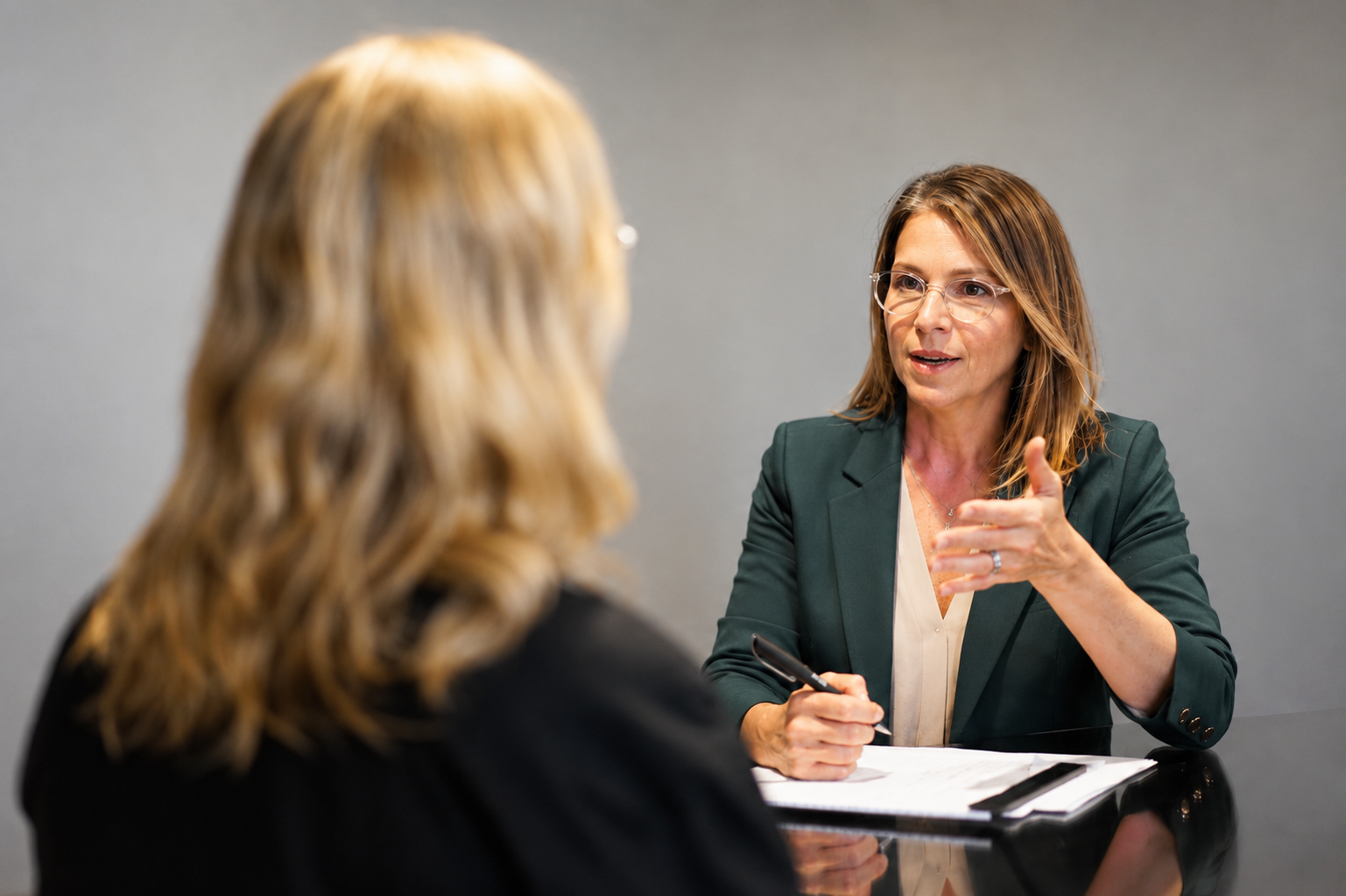 Two women engaged in a discussion at a meeting, one is speaking and the other is listening, with notebooks on the table.
