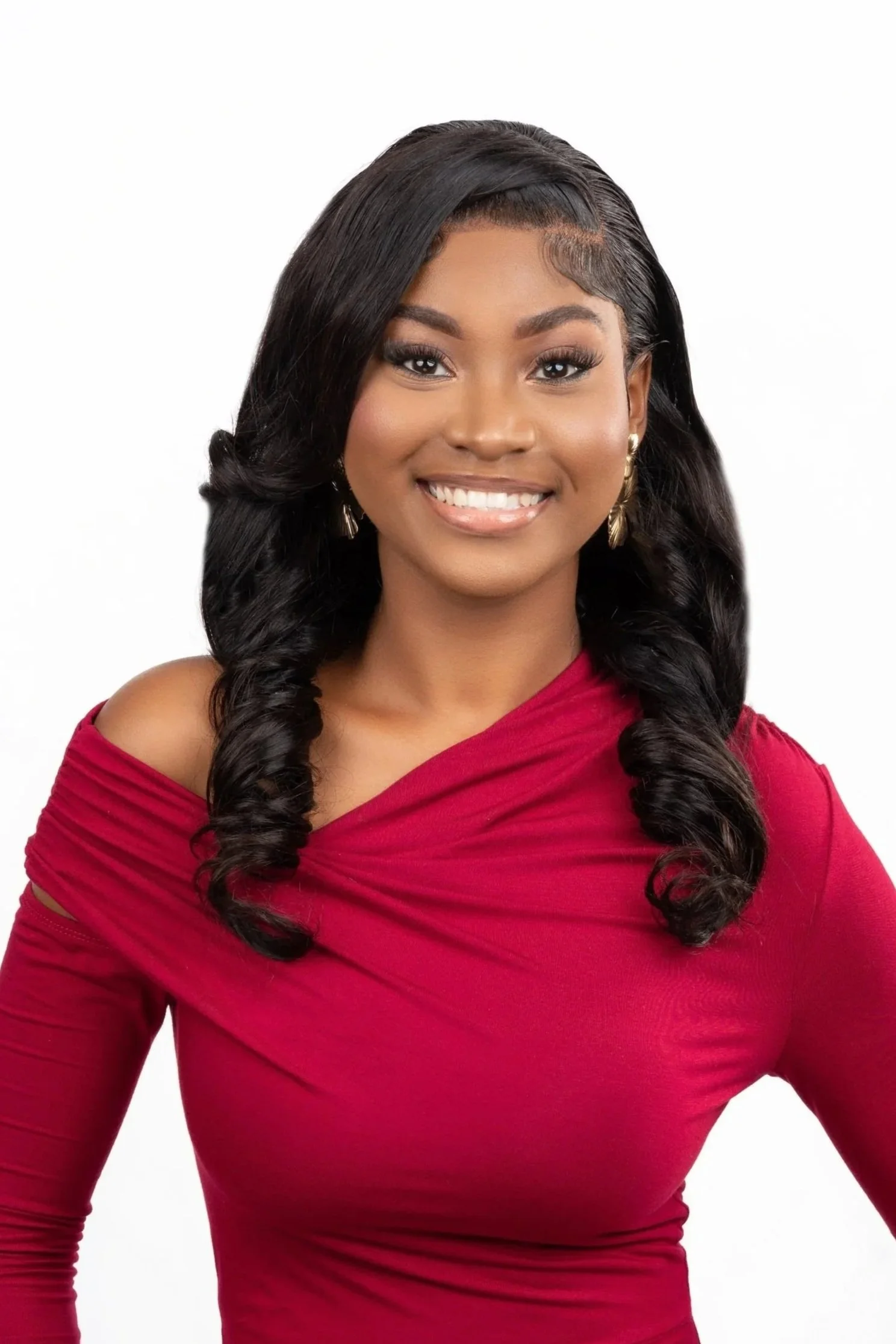 A woman with long black hair styled in loose curls, wearing gold earrings and a red off-the-shoulder dress, smiling against a white background.