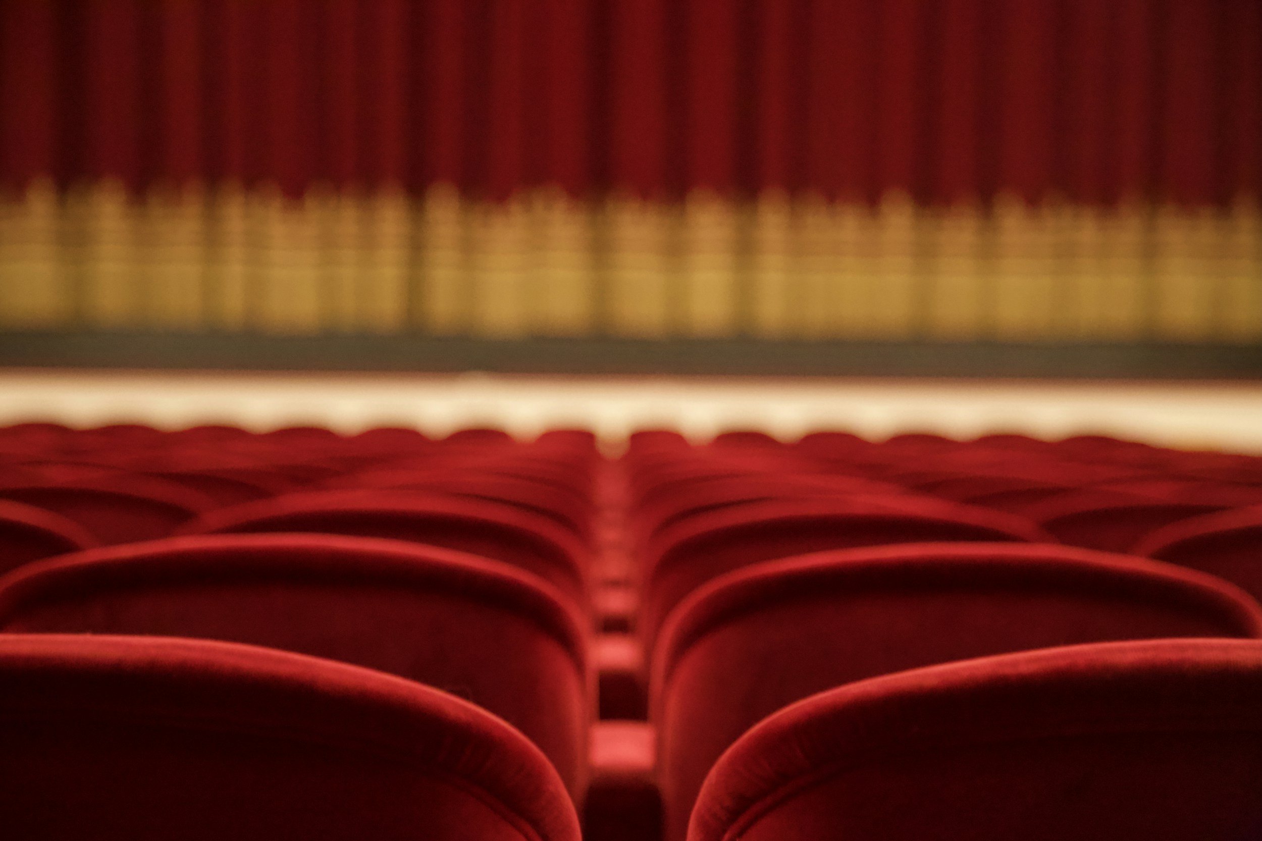 A blurry image of red theater seats from the perspective of the stage.