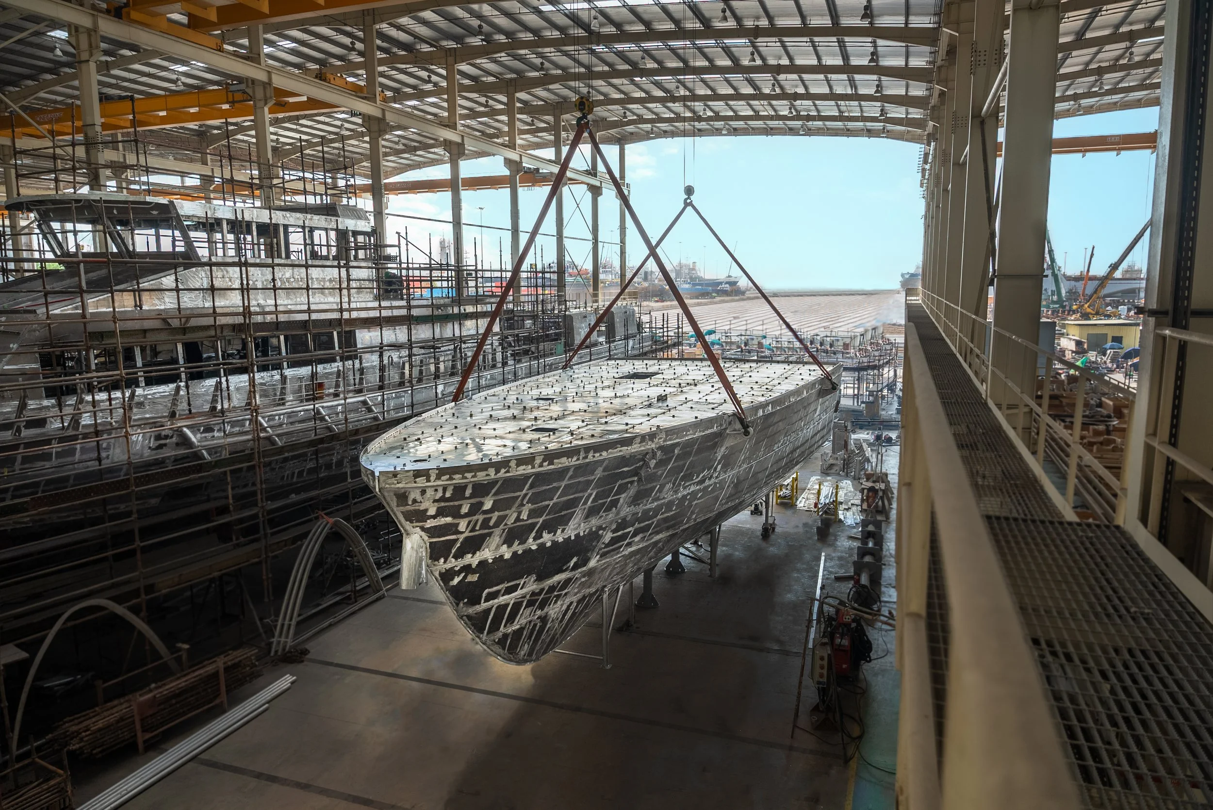 View of a large ship under construction inside a shipyard, with scaffolding, cranes, and a partially built hull visible.