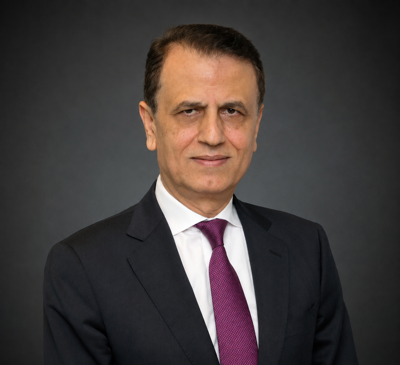 A middle-aged man with brown hair, wearing a dark suit, white shirt, and purple tie, posing against a dark gradient background.