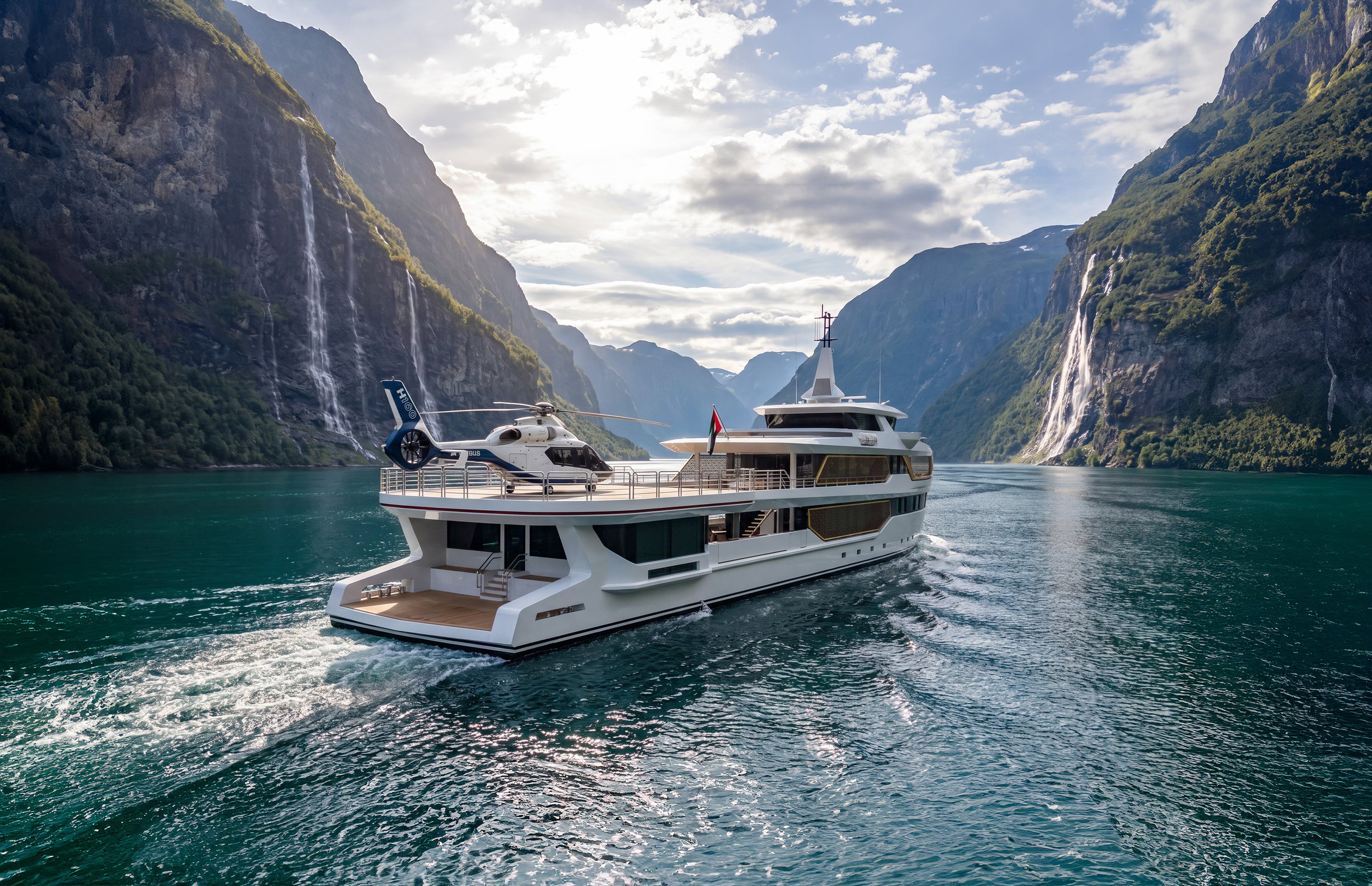A luxury yacht with a helicopter parked on the deck, sailing through a fjord with tall, green mountains on either side and waterfalls cascading down the cliffs.